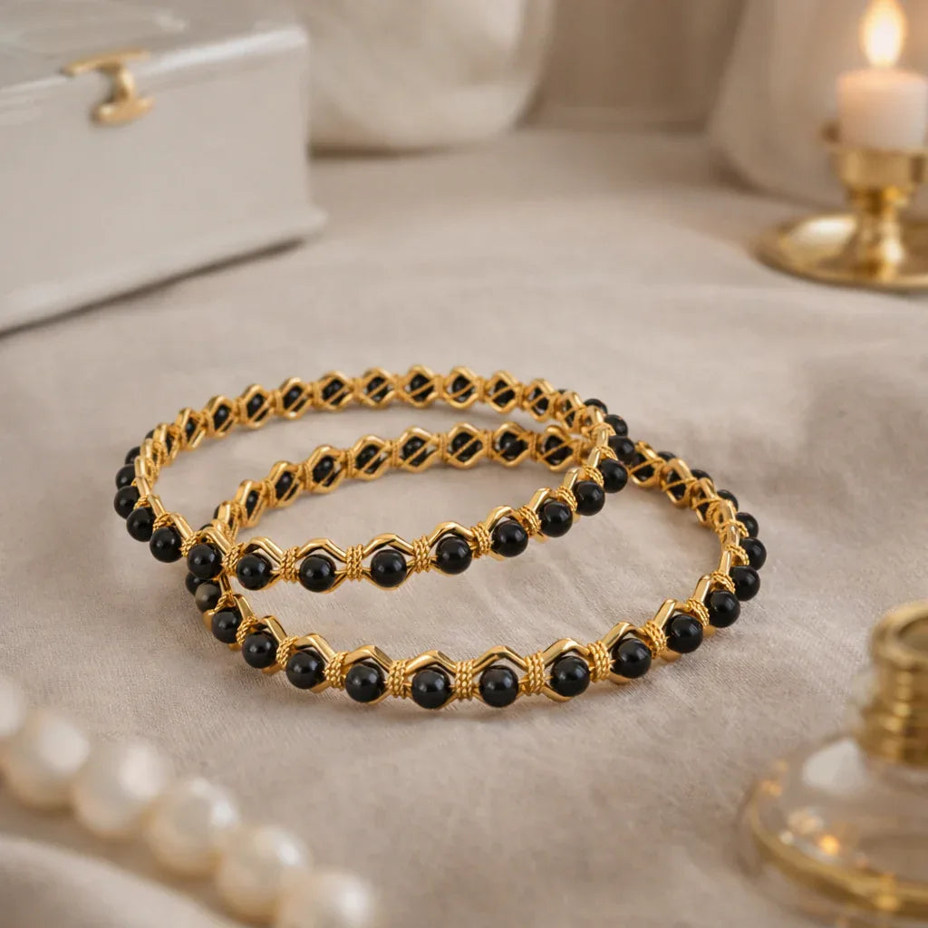 Gold and black beaded bracelets on a textured surface with a candle and jewelry box in the background.