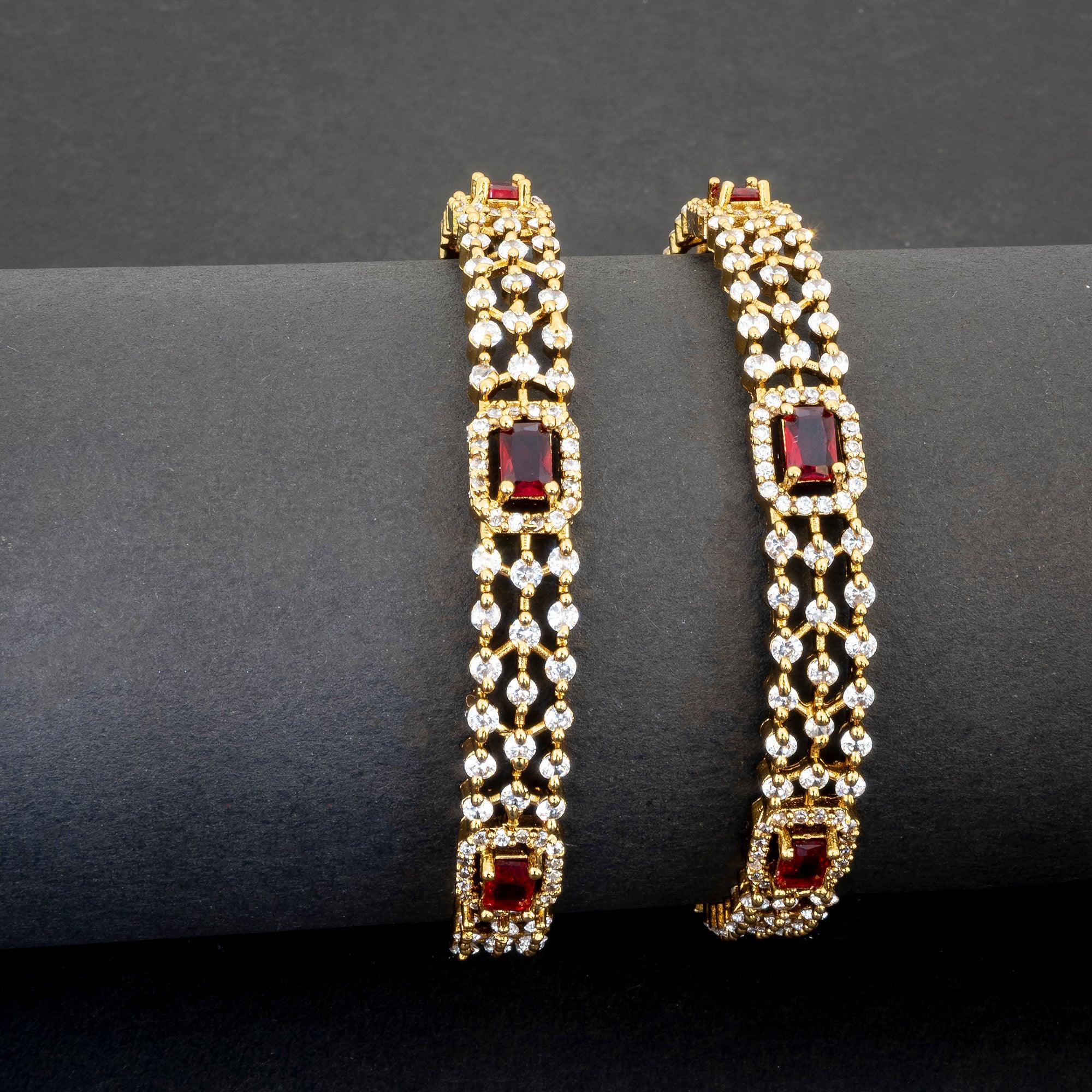 Pair of gold bracelets with red gemstones on a dark surface