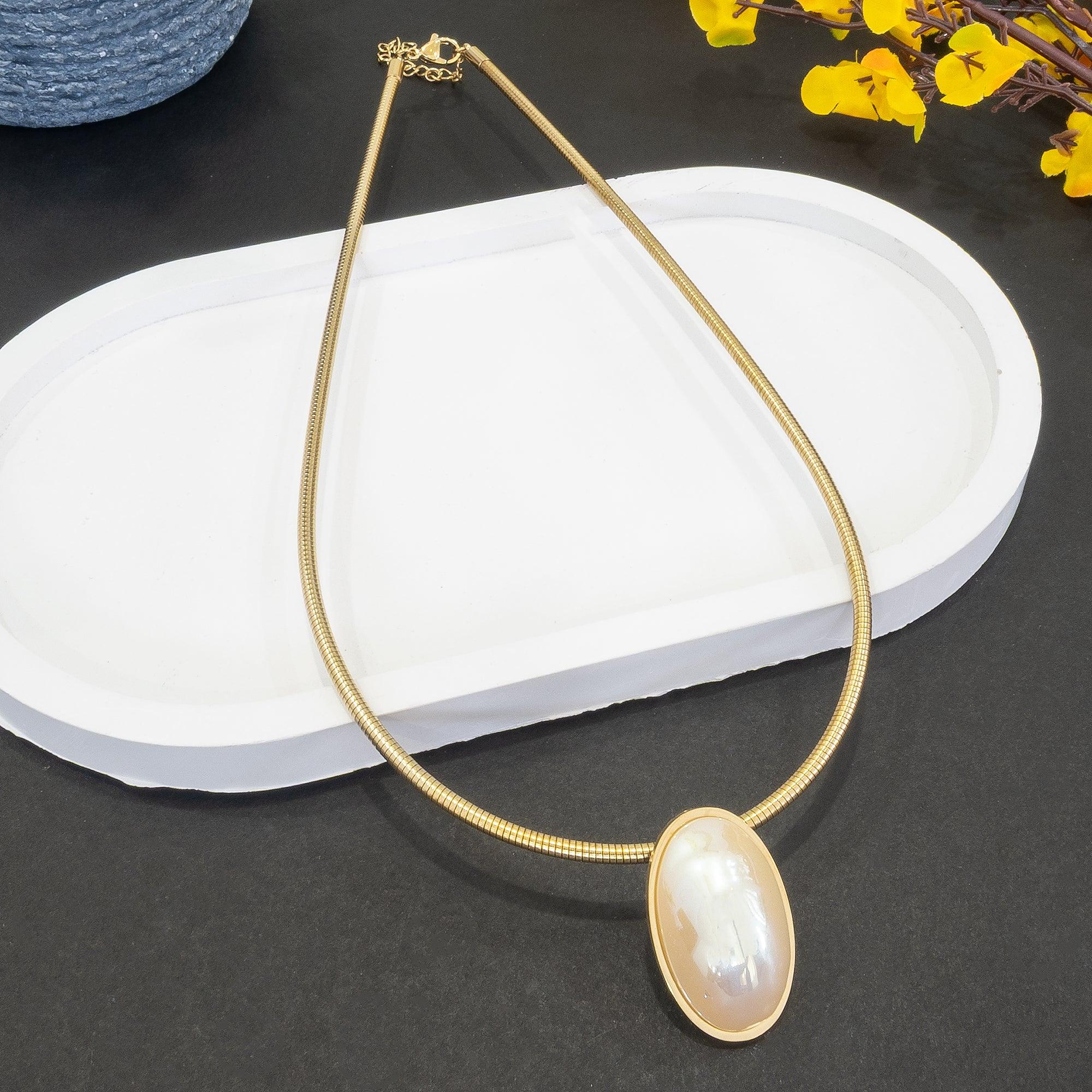 Gold necklace with a large pendant on a dark surface with yellow flowers.