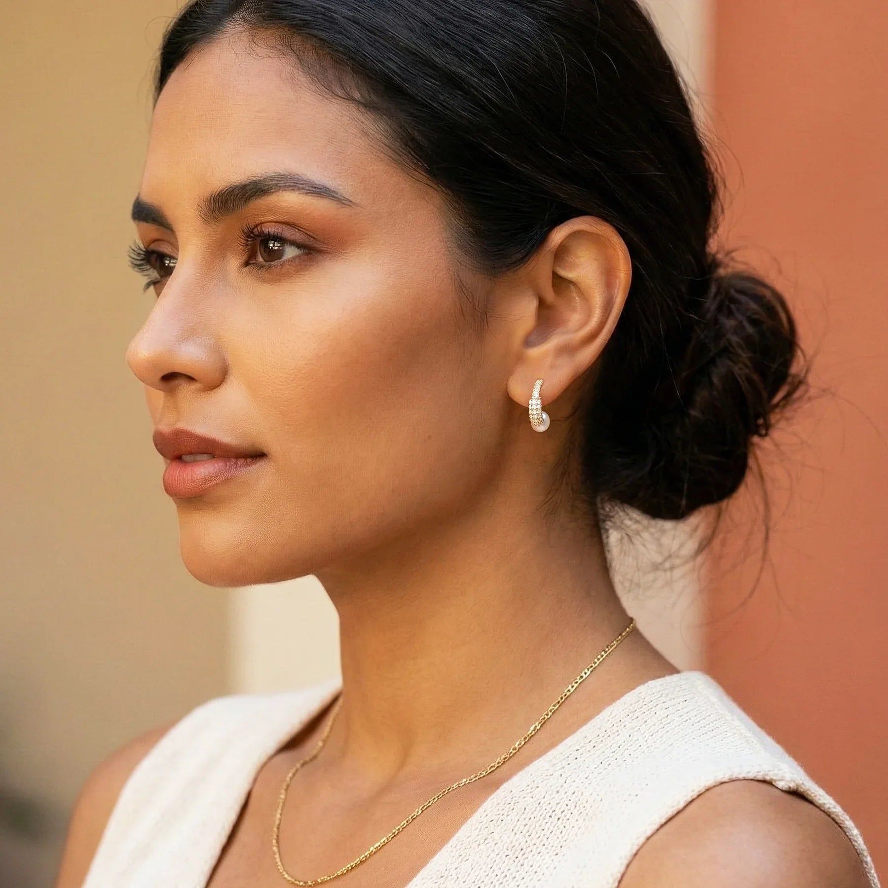 Woman wearing a gold necklace and earrings with a neutral background