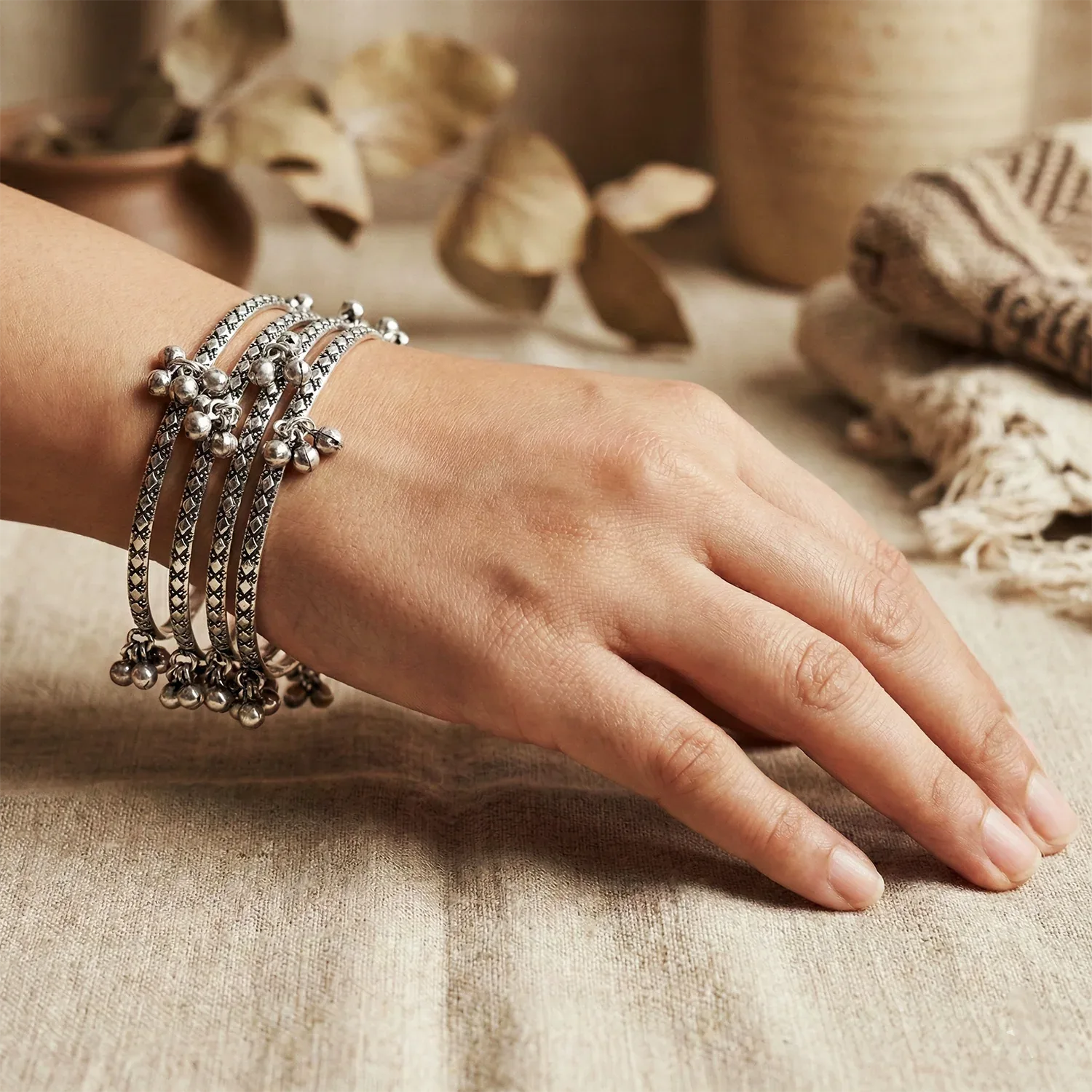 Hand wearing multiple silver bracelets on a textured surface with natural elements in the background