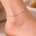 Ankle bracelet with blue beads and pearls on a foot against a neutral background