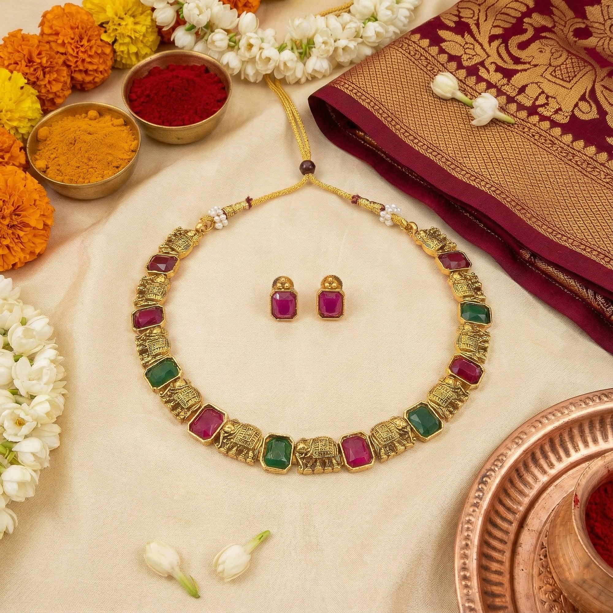 Gold necklace with colorful stones and matching earrings on a decorative background with flowers and a saree.