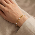 Gold bracelet with pearls on a wrist against a beige background