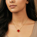 Close-up of a woman wearing a gold necklace with a red clover pendant.