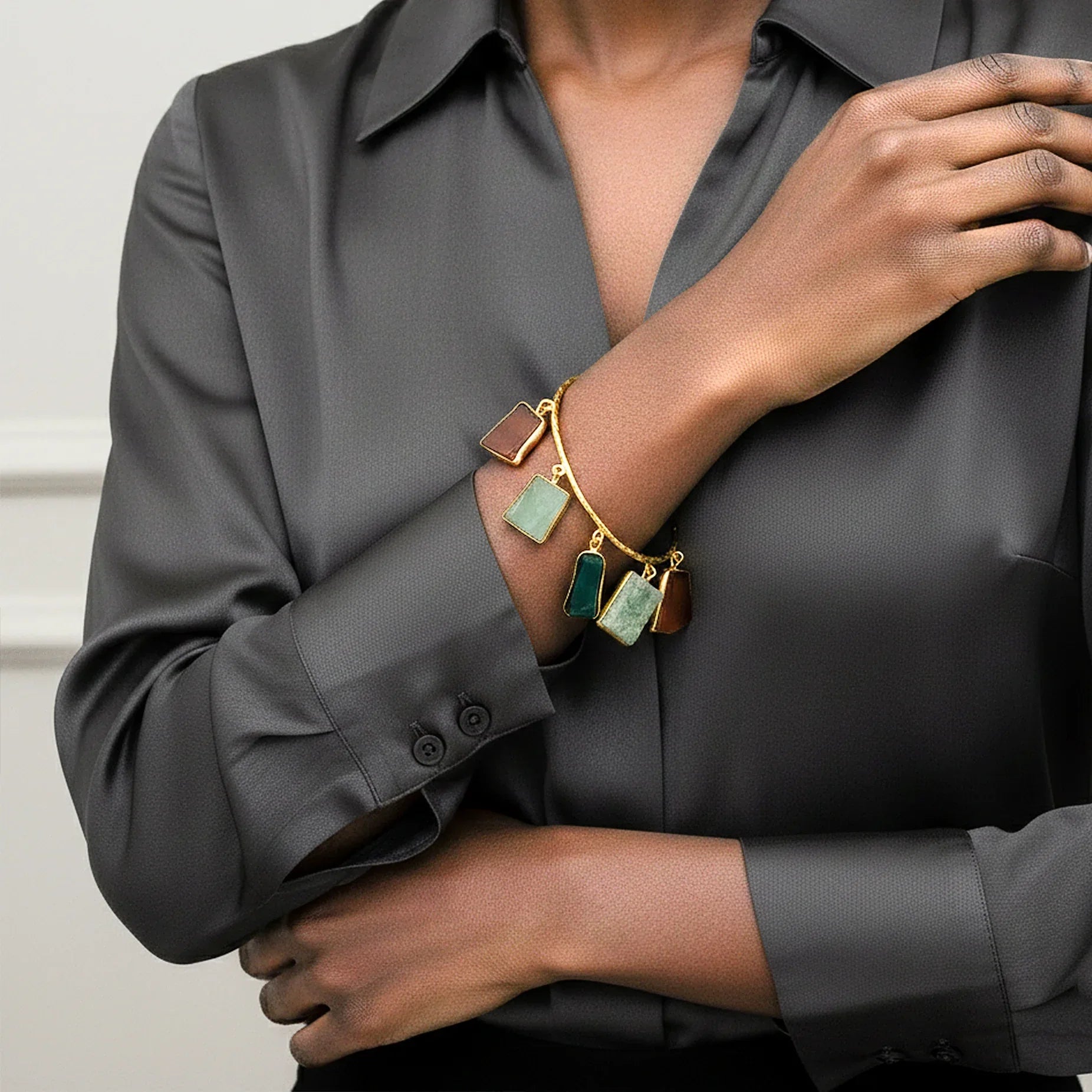 Person wearing a gold bracelet with green gemstones on a gray shirt.