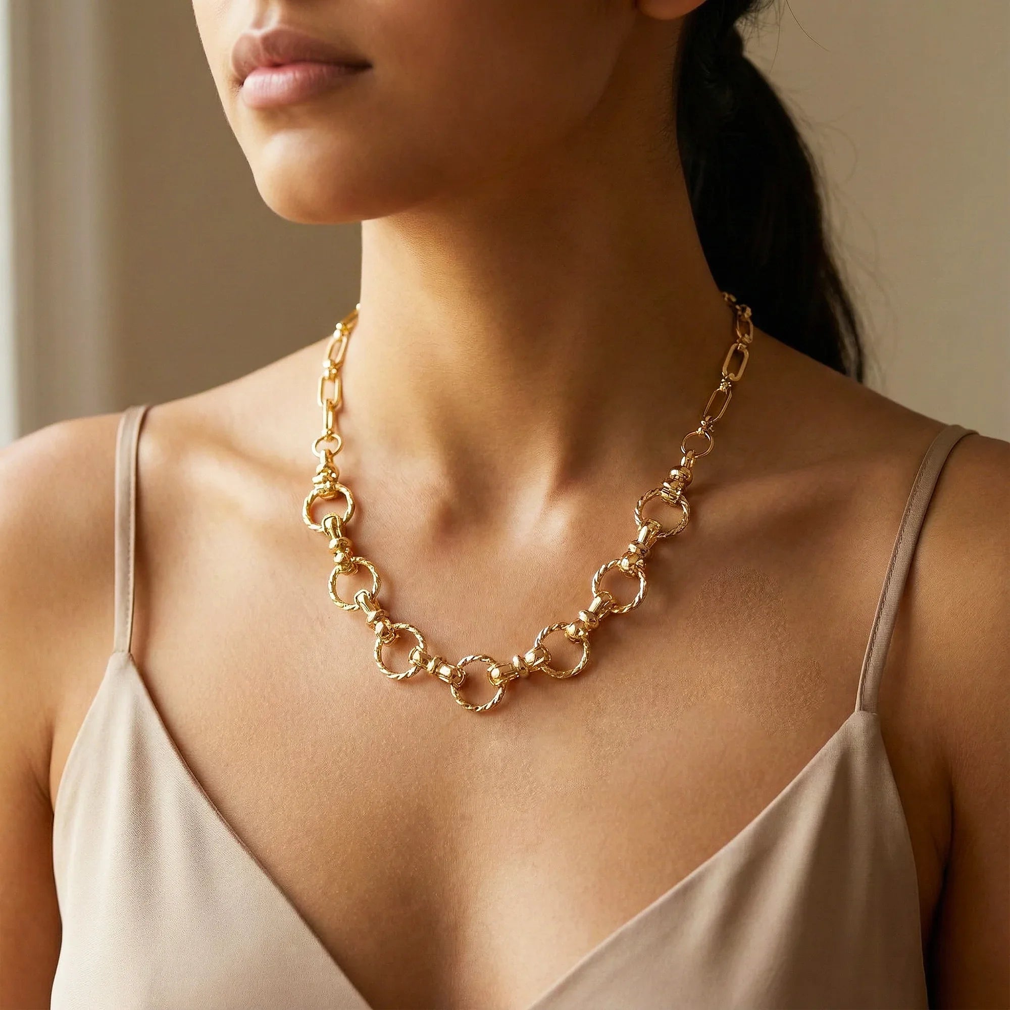 Woman wearing a gold chain necklace with a neutral background