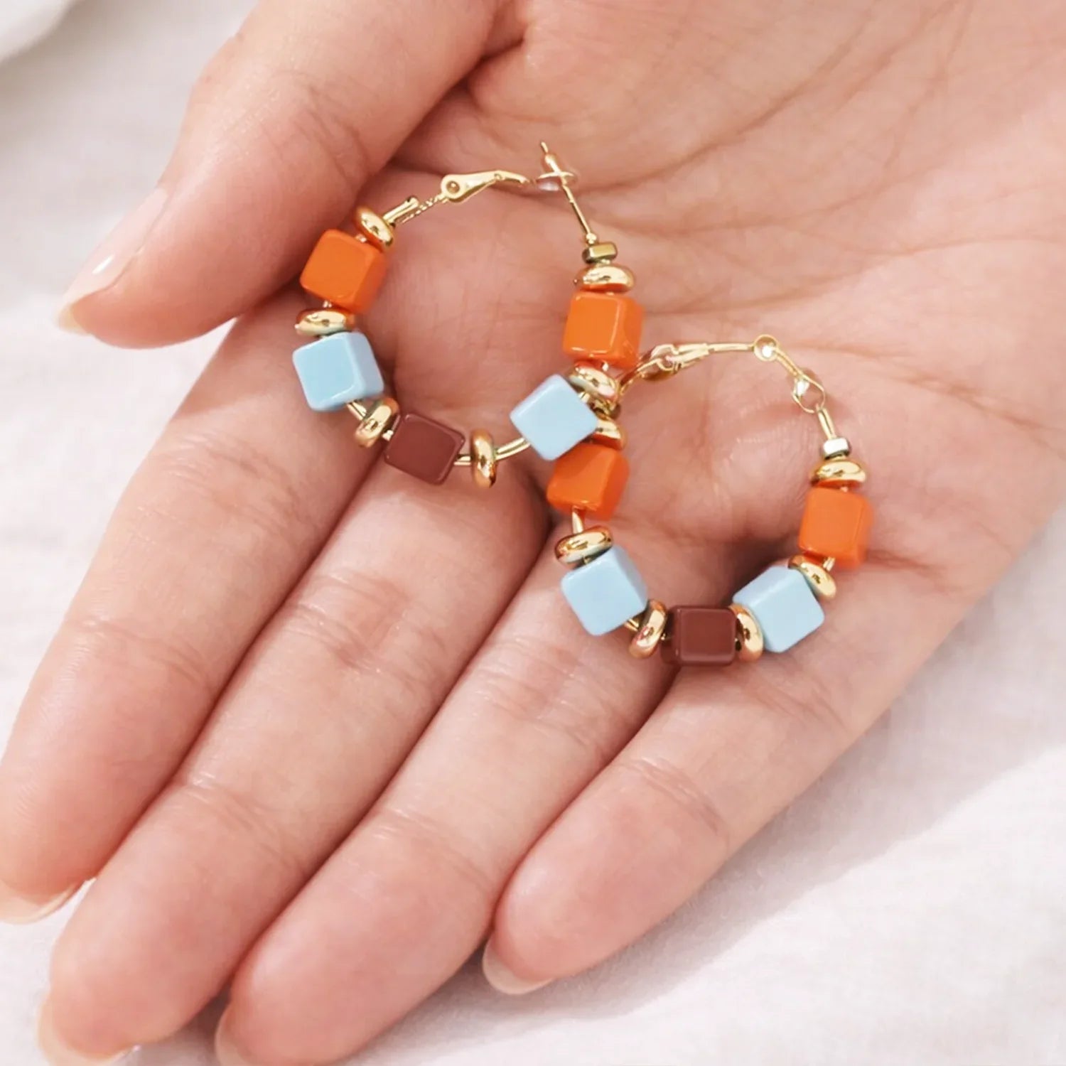 Colorful beaded earrings held in a hand against a neutral background