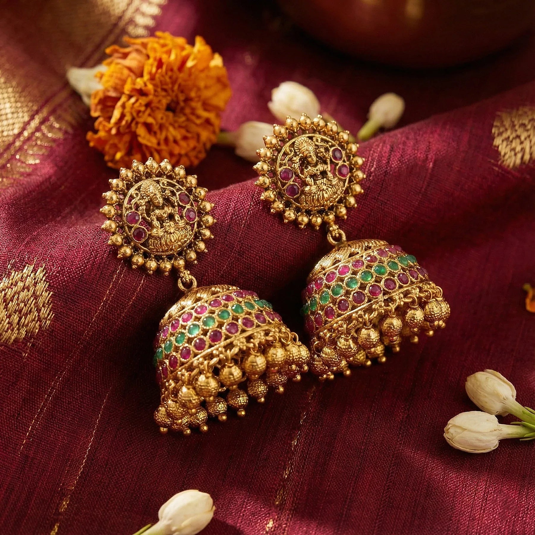 Gold earrings with gemstones on a maroon fabric background