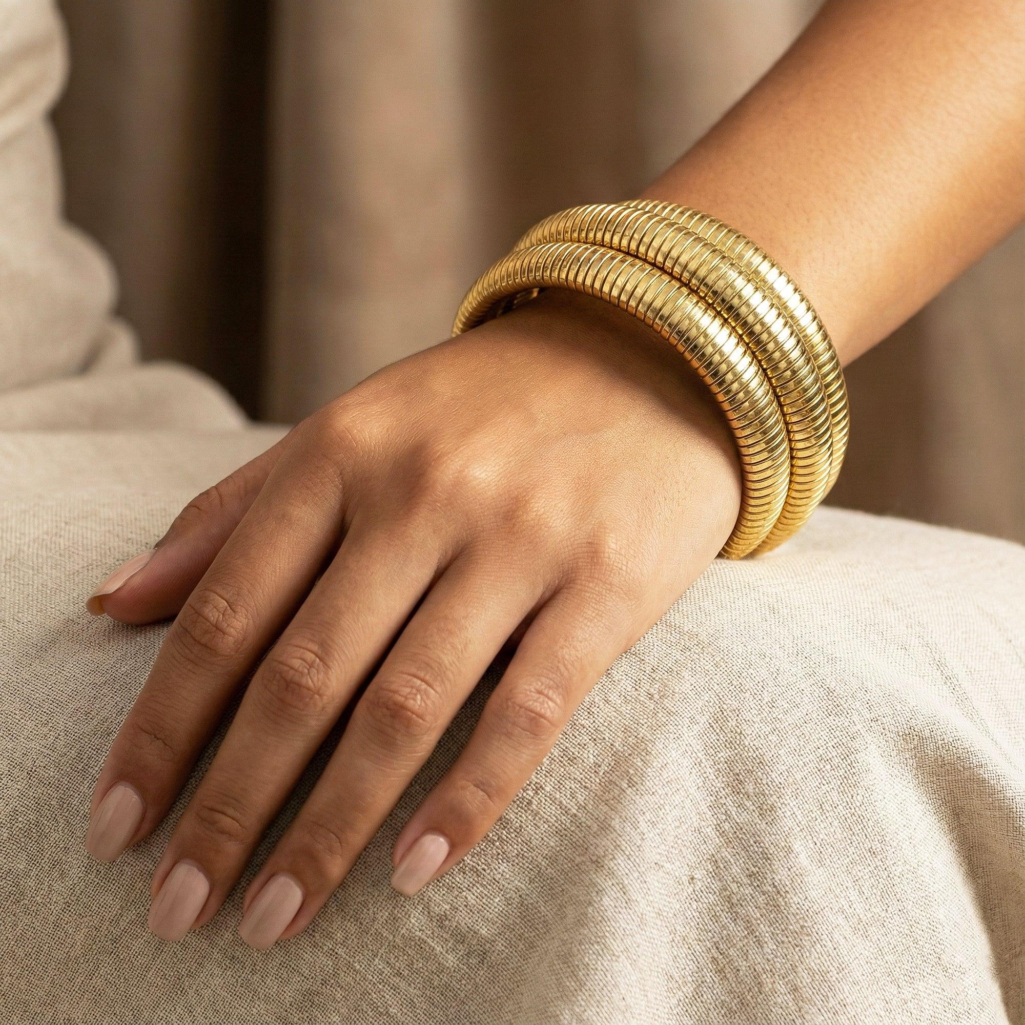 Hand wearing multiple gold bracelets on a neutral background