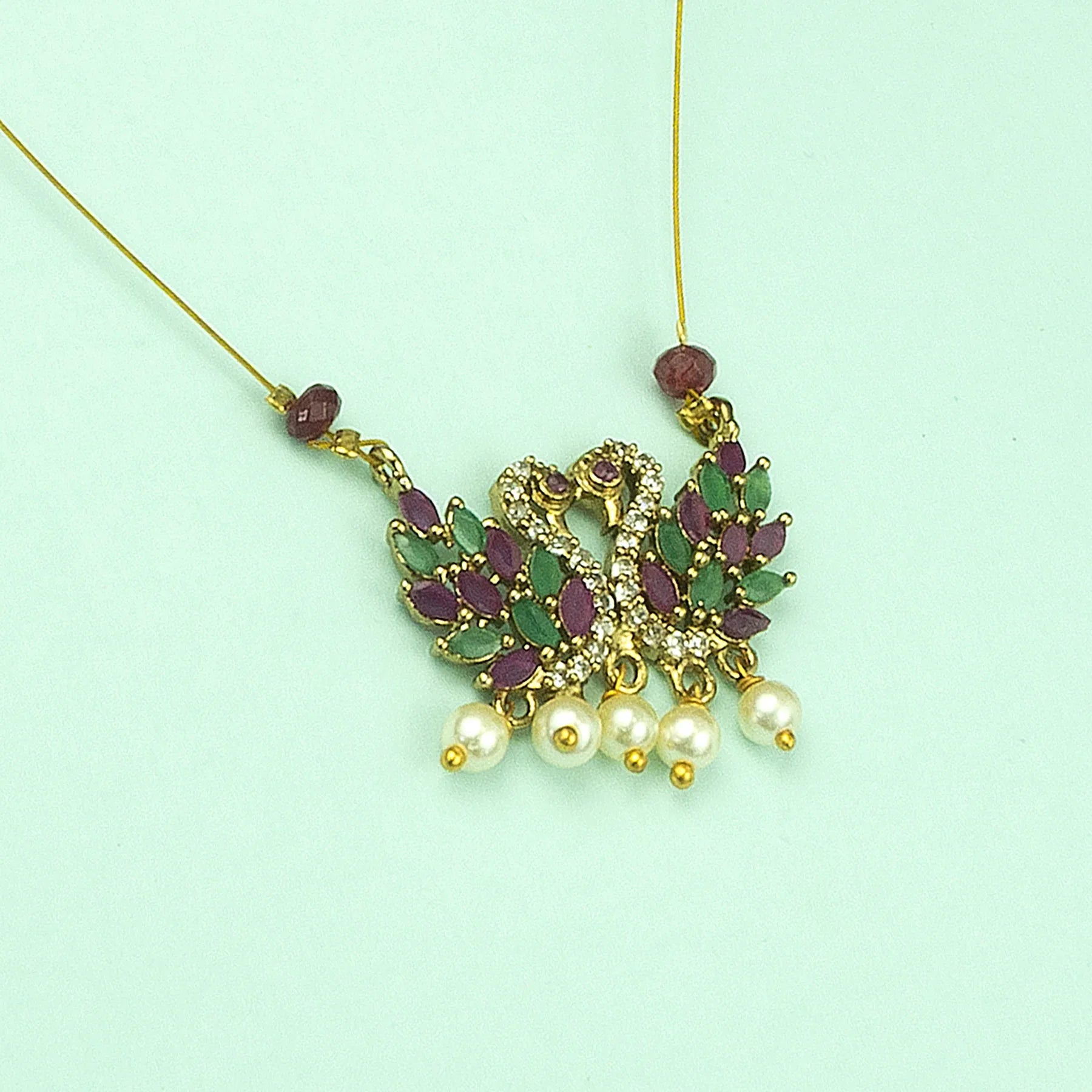 Gold necklace with green and purple stones and pearl-like beads on a light green background