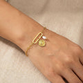 Gold bracelet with a coin charm and pearl on a wrist against a beige background