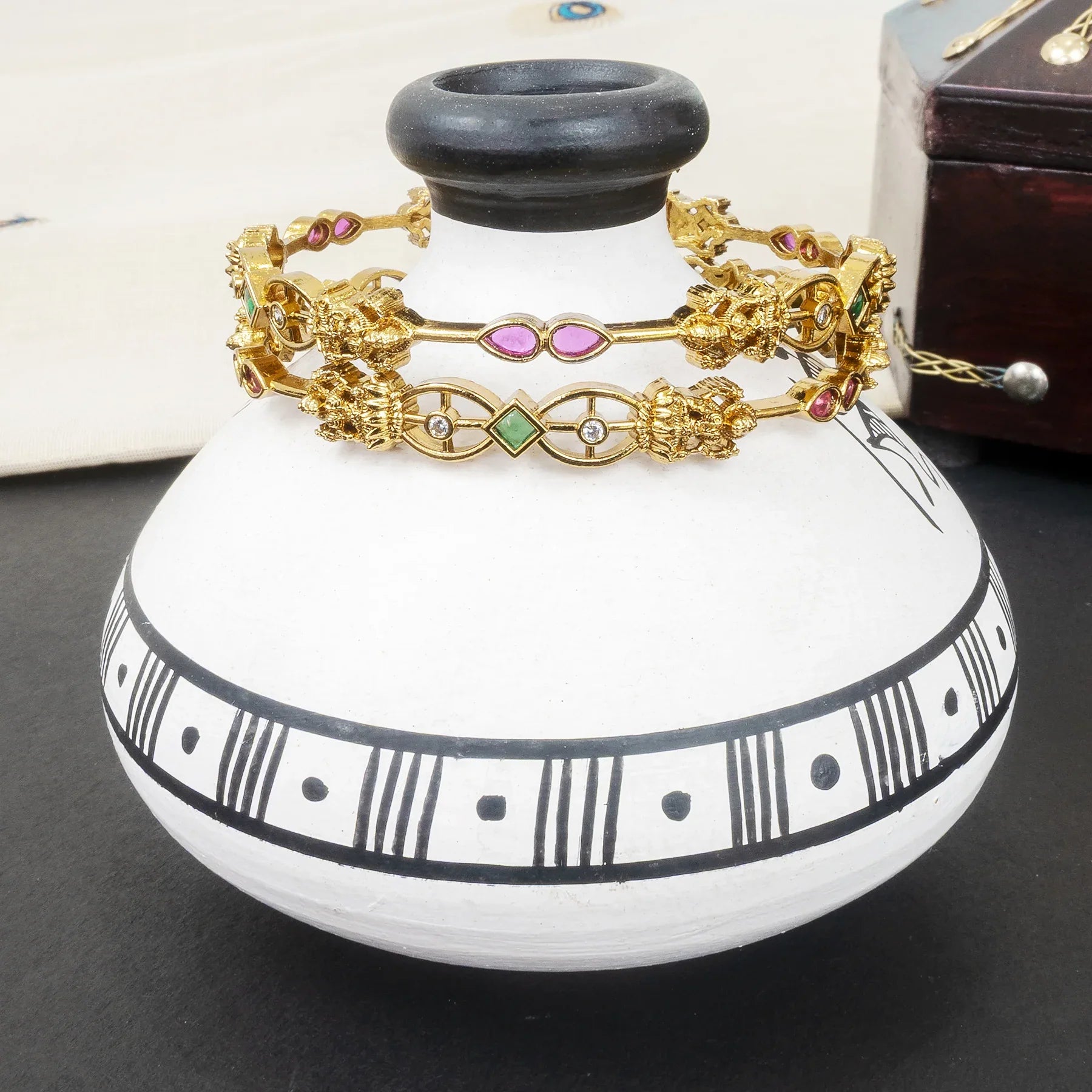 Gold bracelets with colorful stones on a white vase with black patterns