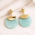 Gold and light blue earrings on a white fabric background