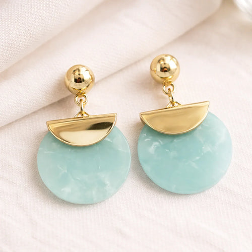 Gold and light blue earrings on a white fabric background