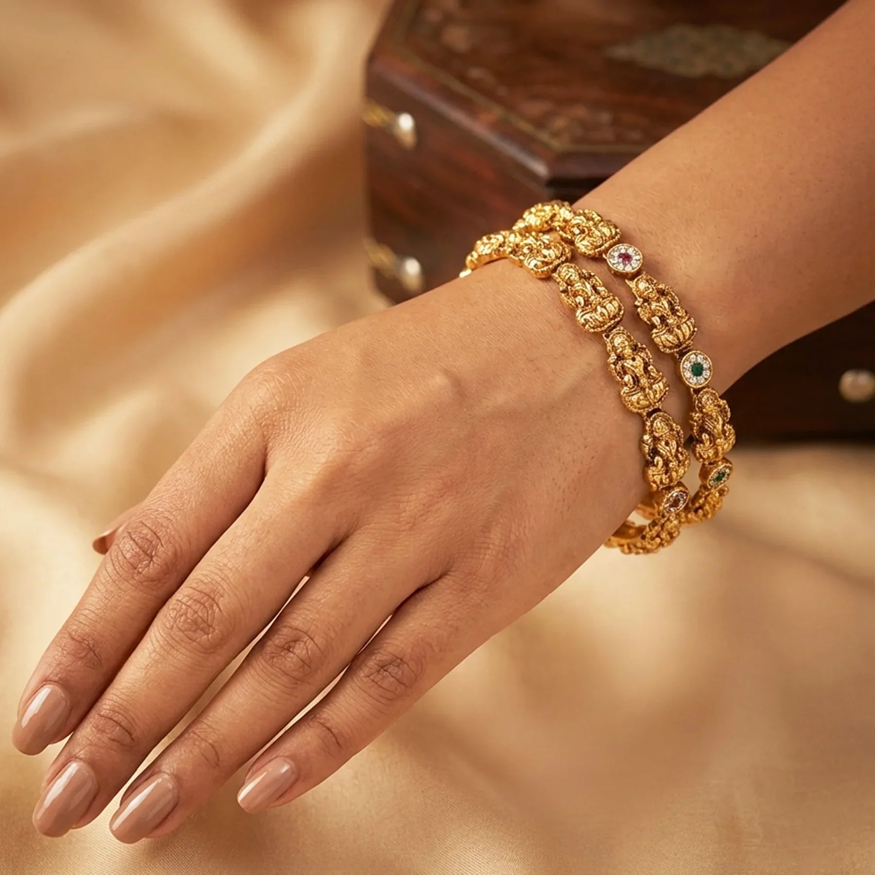 Gold bracelet with gemstones on a hand against a soft, neutral background