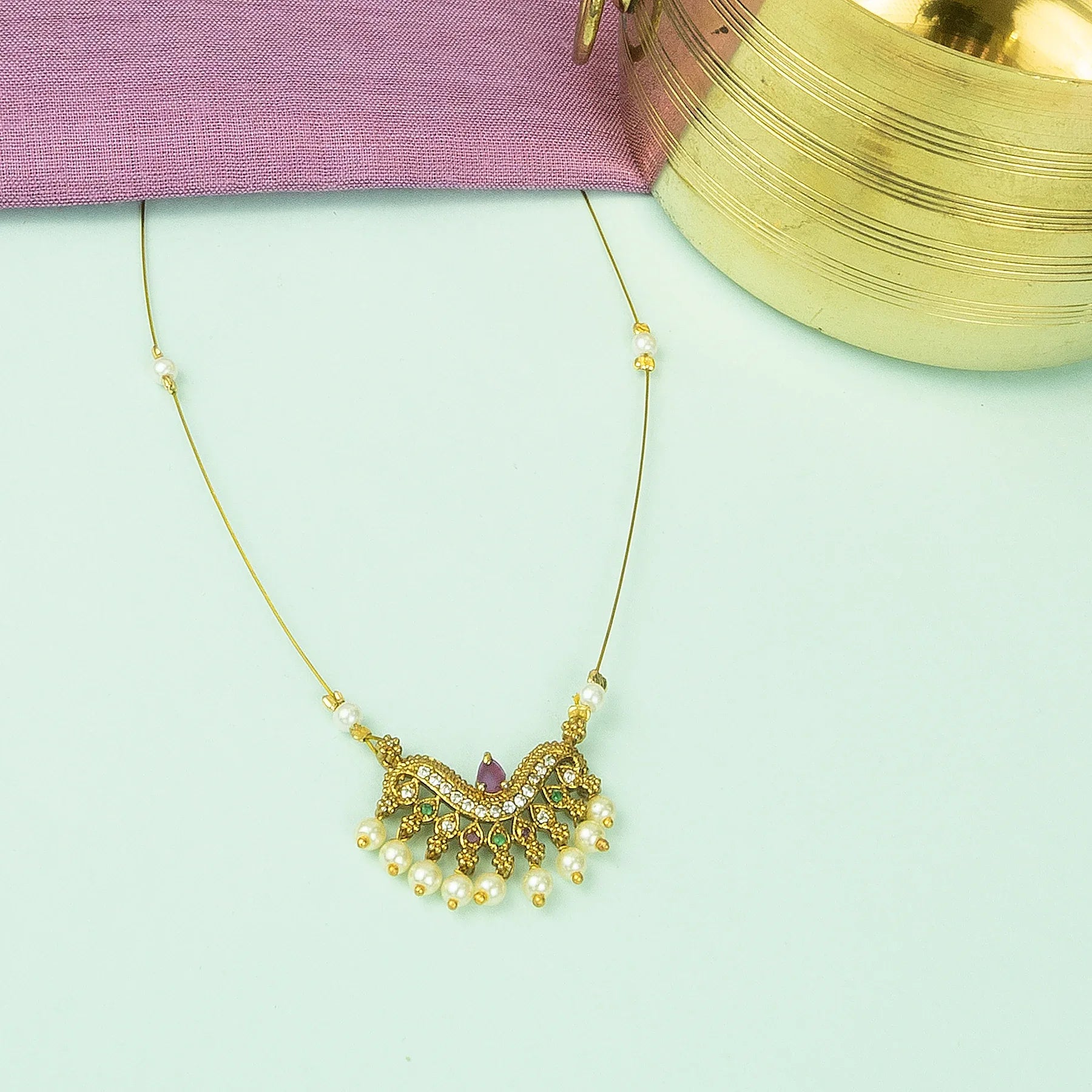 Gold necklace with pearls and gemstones on a light green background