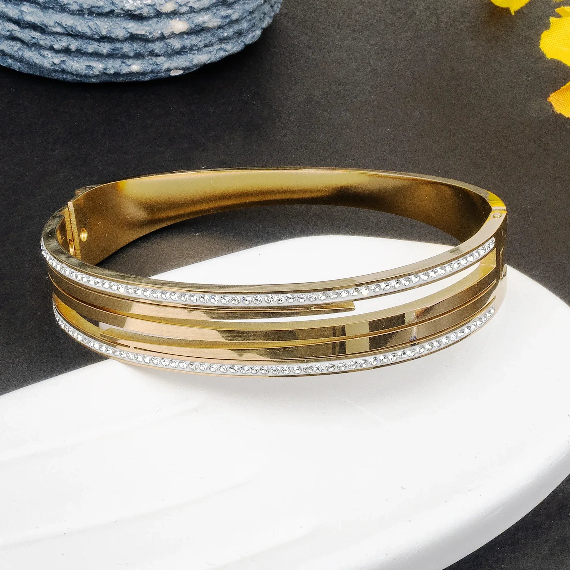 Gold bracelet with rhinestones on a white plate against a dark background