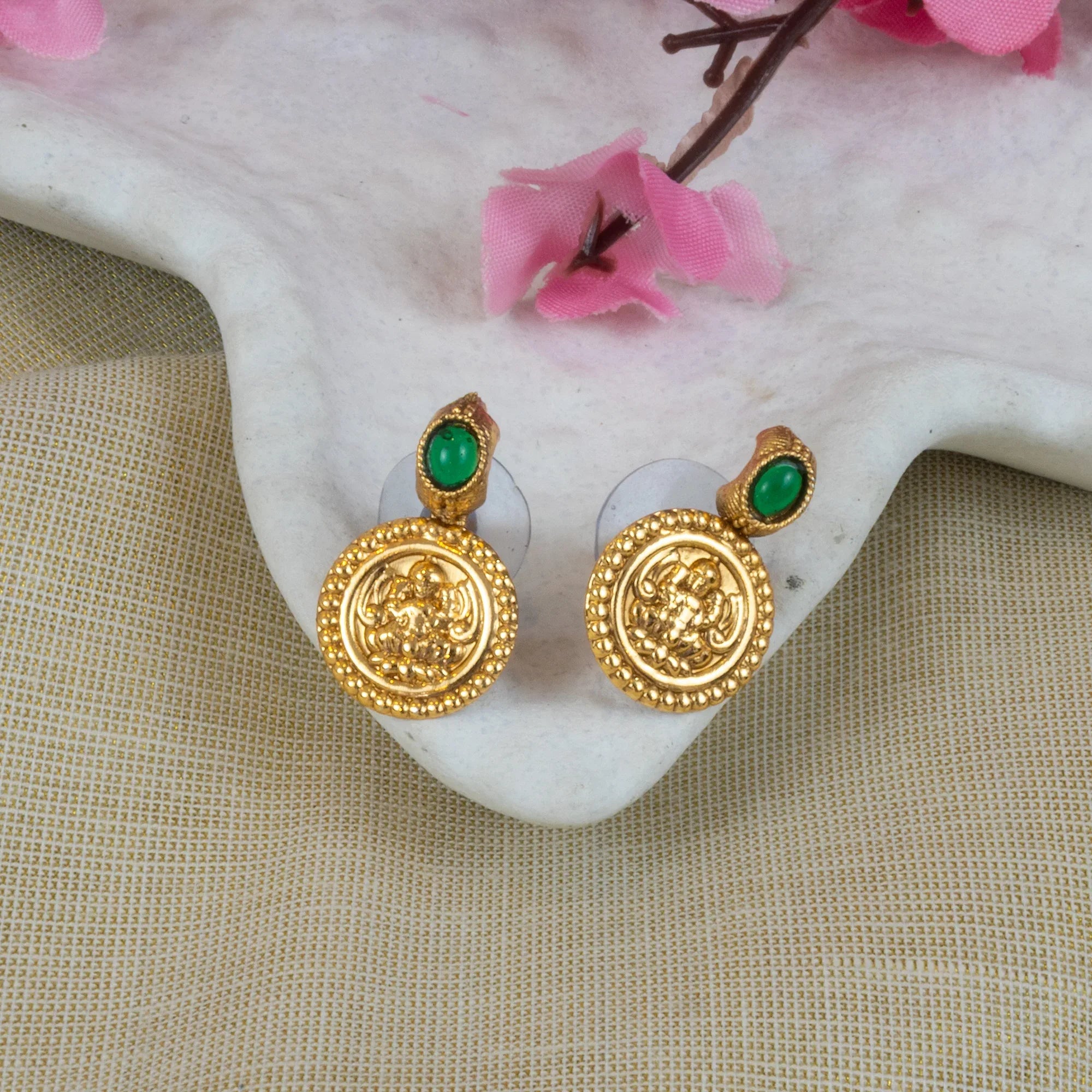 Gold earrings with green gemstones on a shell with pink flowers