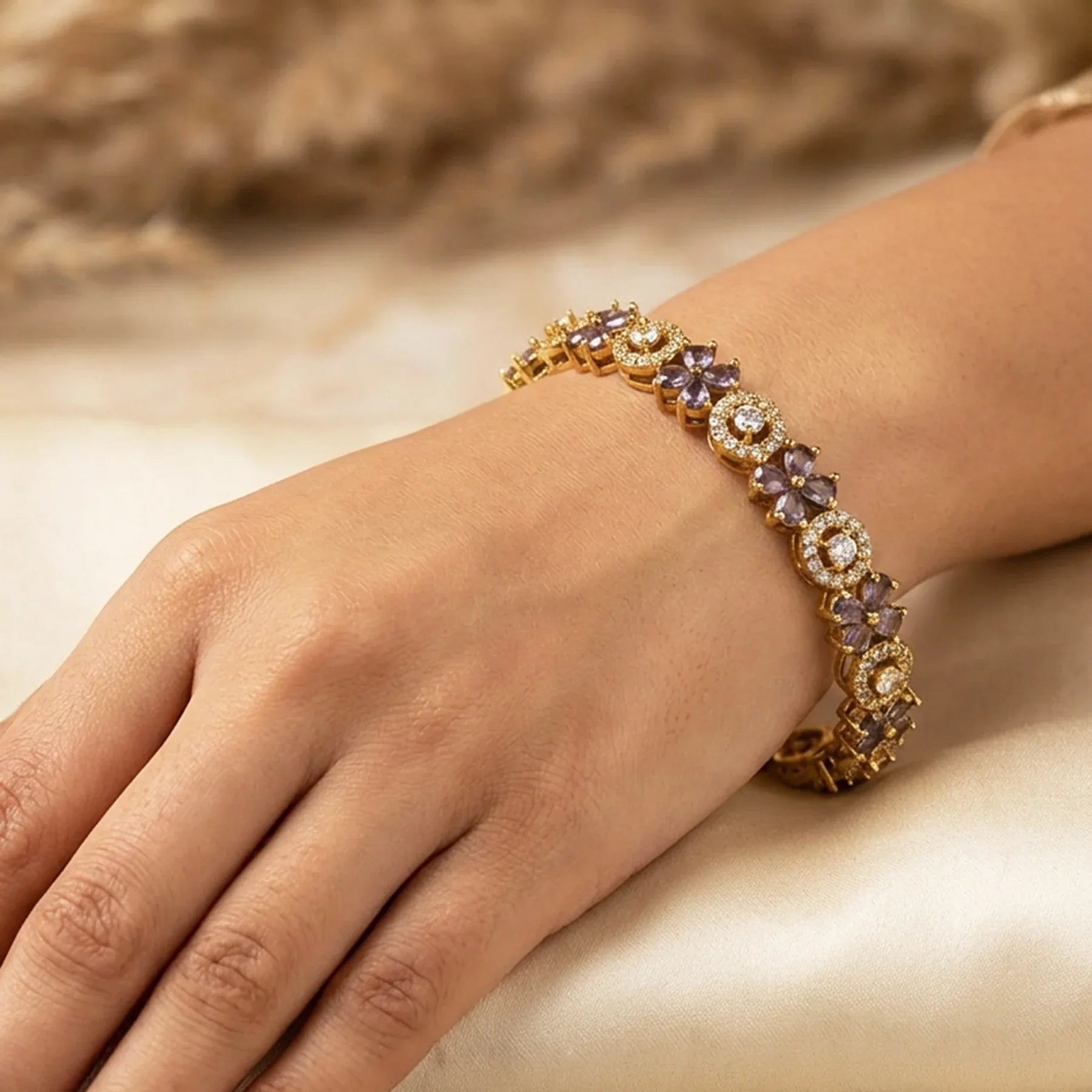 Gold bracelet with purple stones on a hand against a neutral background