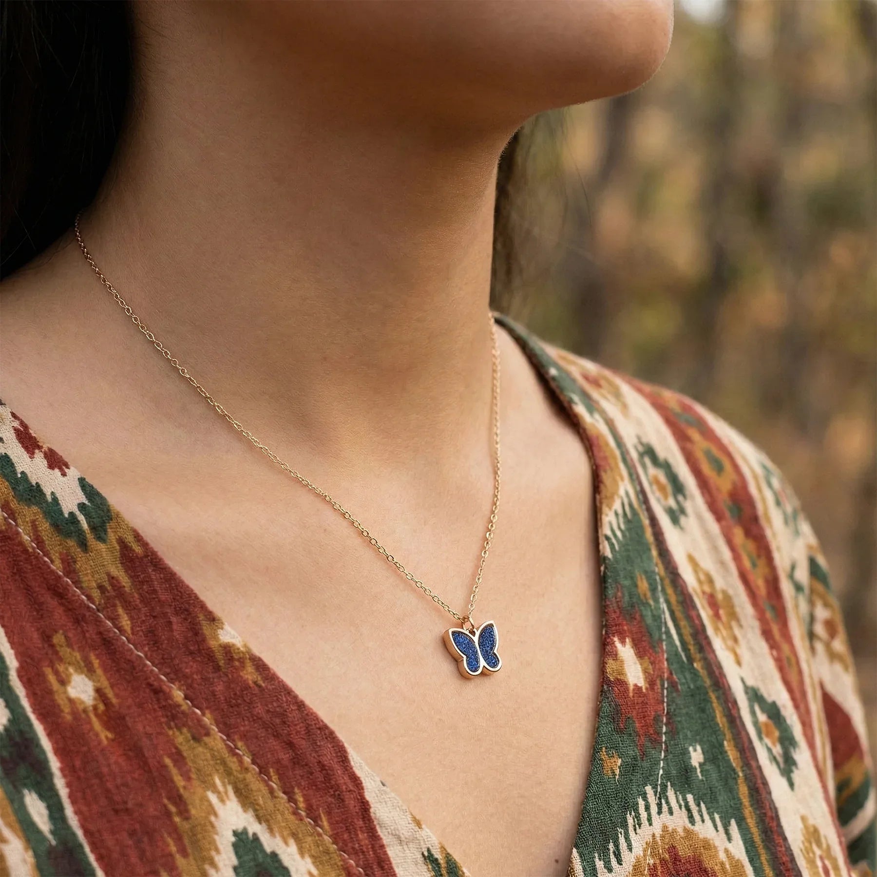 Person wearing a gold necklace with a blue butterfly pendant, outdoors.