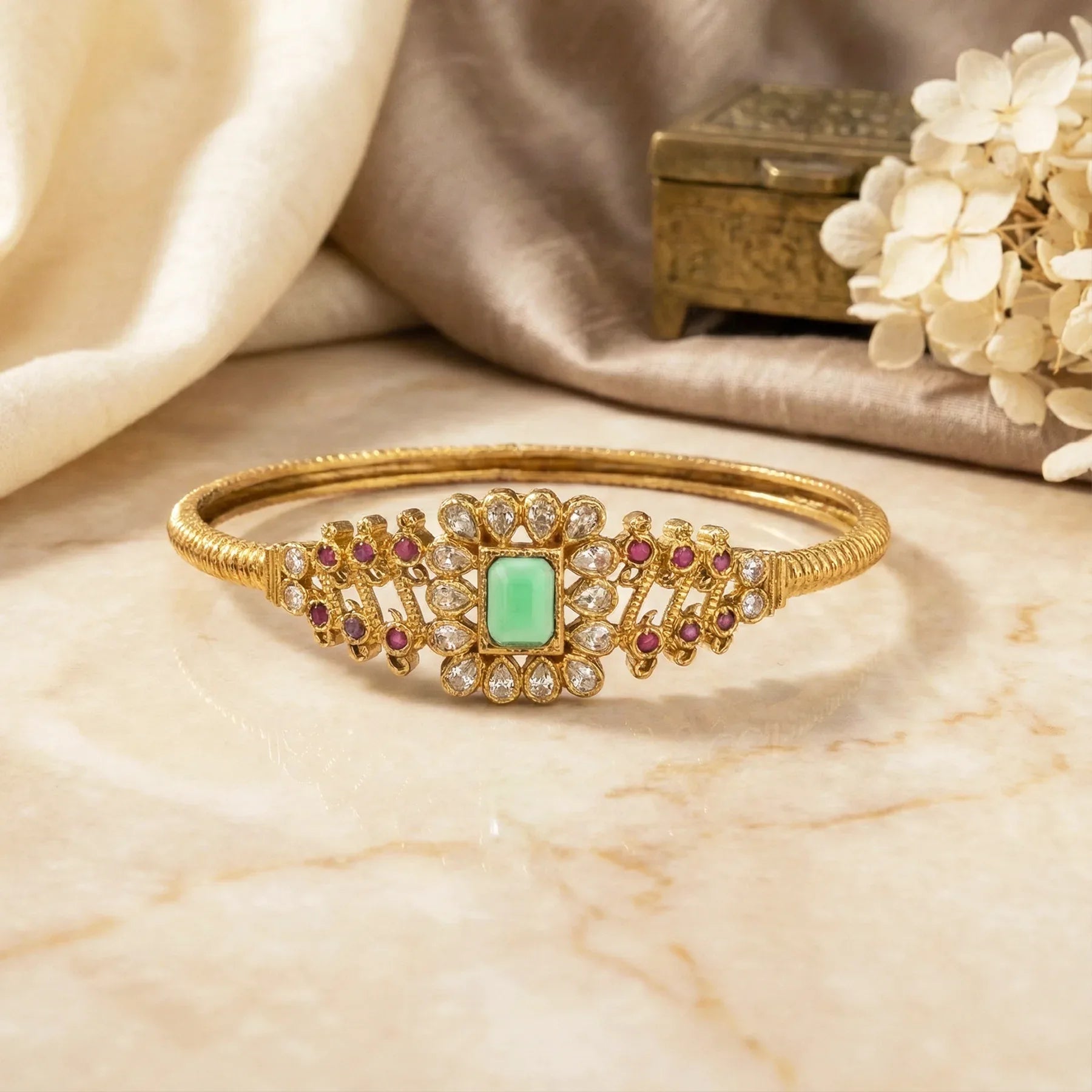 Gold bracelet with green gemstone and red stones on a marble surface
