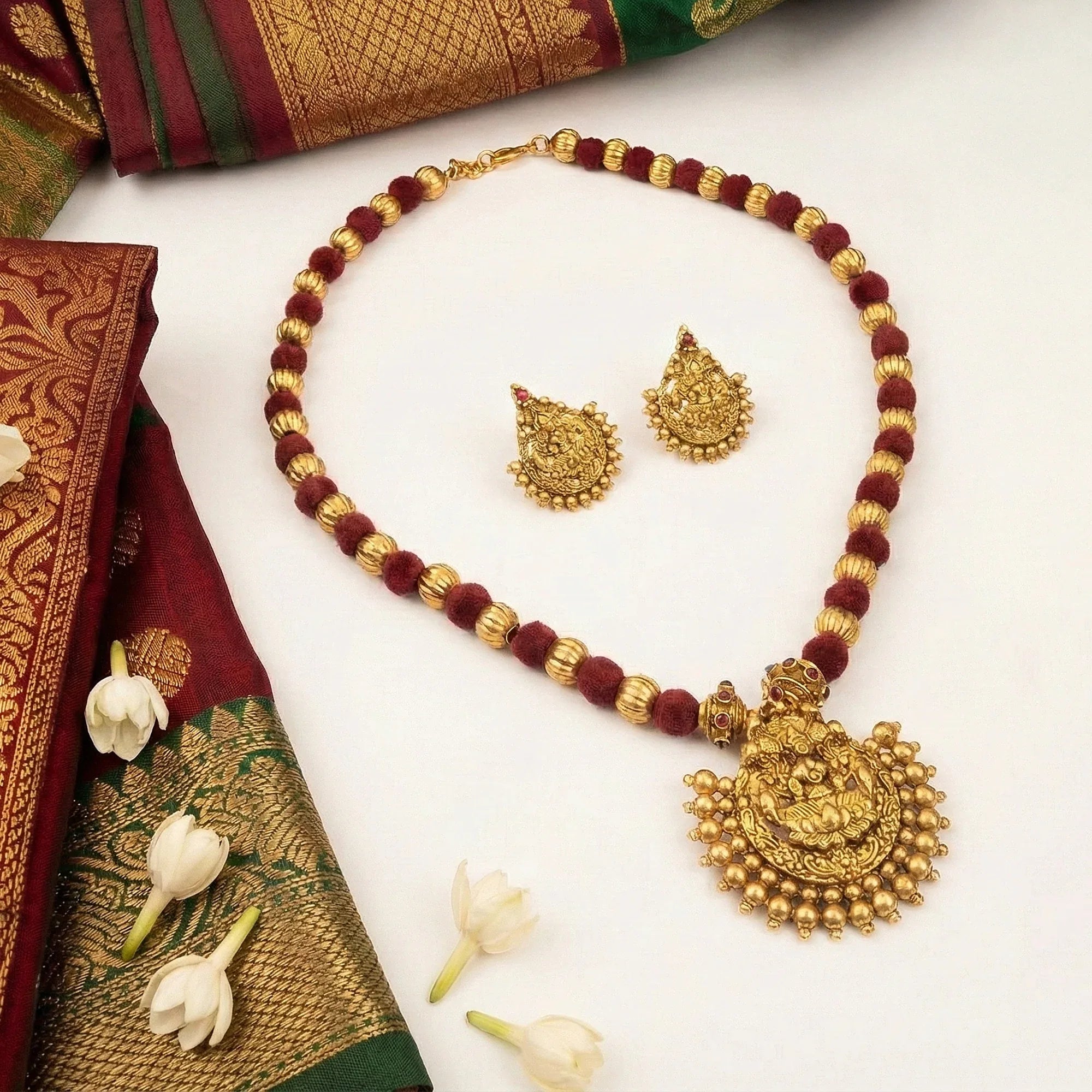 Gold necklace and earrings set with maroon beads on a white background