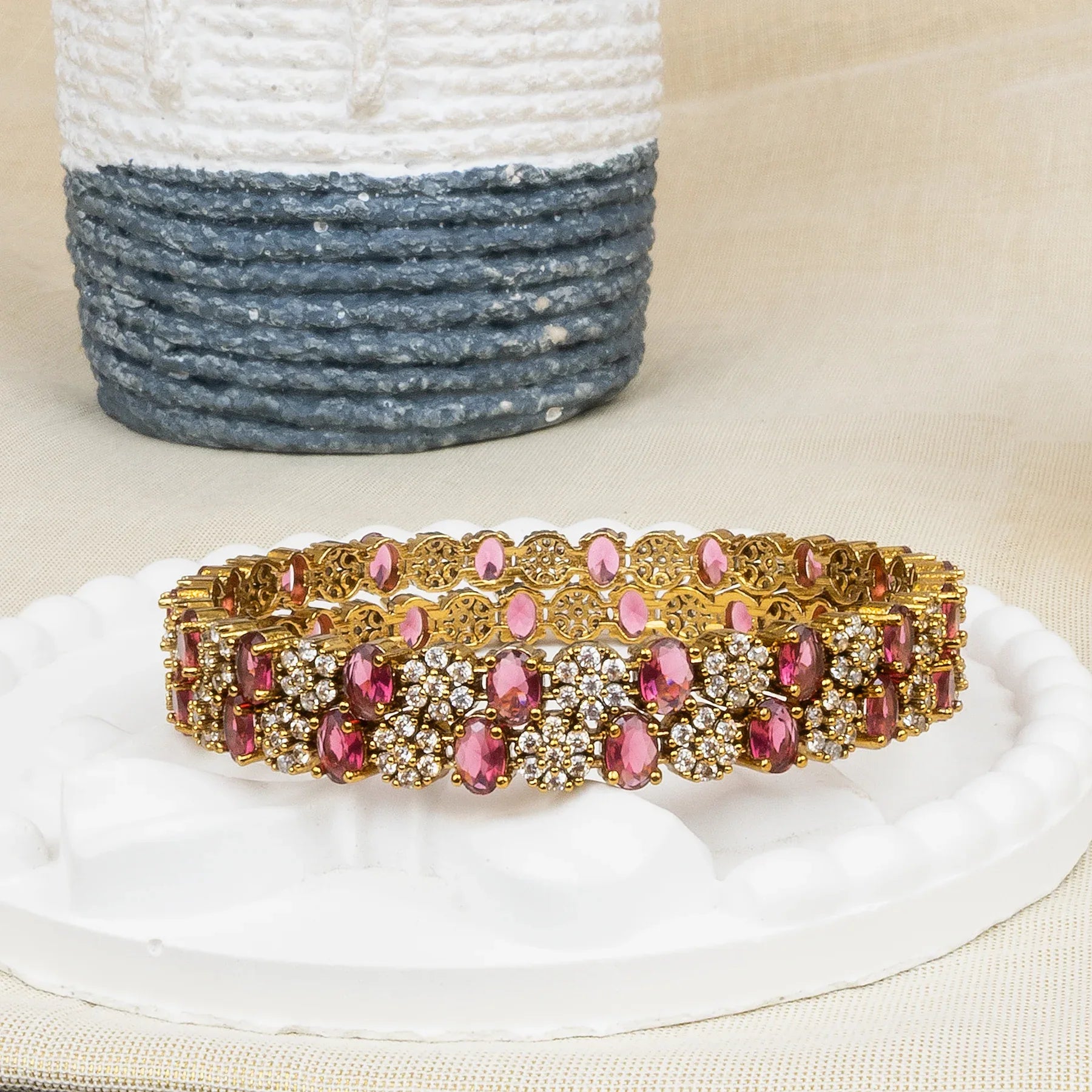 Gold bracelet with pink stones on a white stand with a textured blue and white basket in the background.