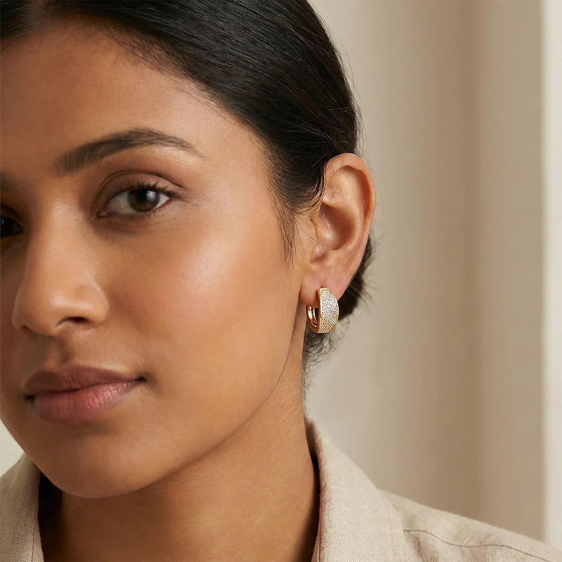 Close-up of a woman wearing gold hoop earrings against a neutral background
