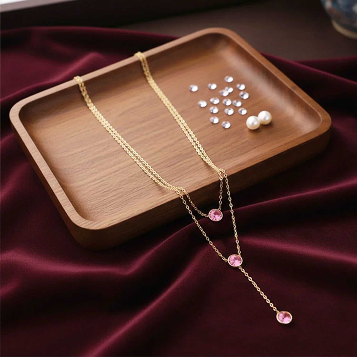Gold necklace with pink gemstones on a wooden tray with pearls on a dark fabric background
