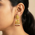 Gold earrings with red and green stones worn by a person