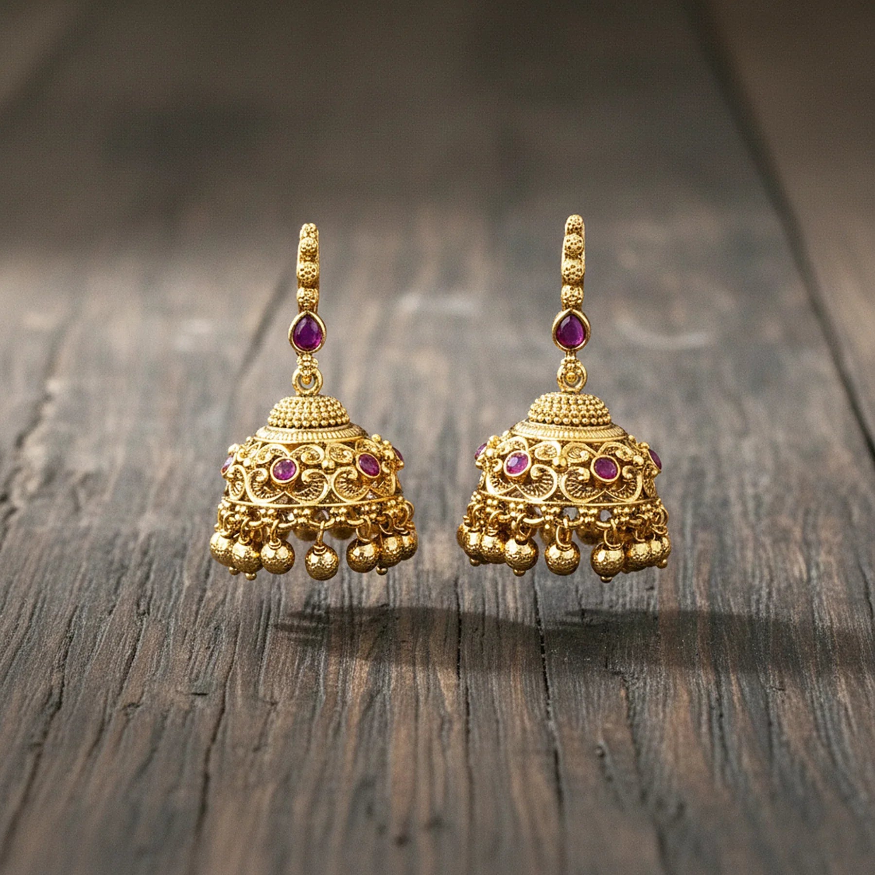 Pair of gold earrings with red gemstones on a wooden surface