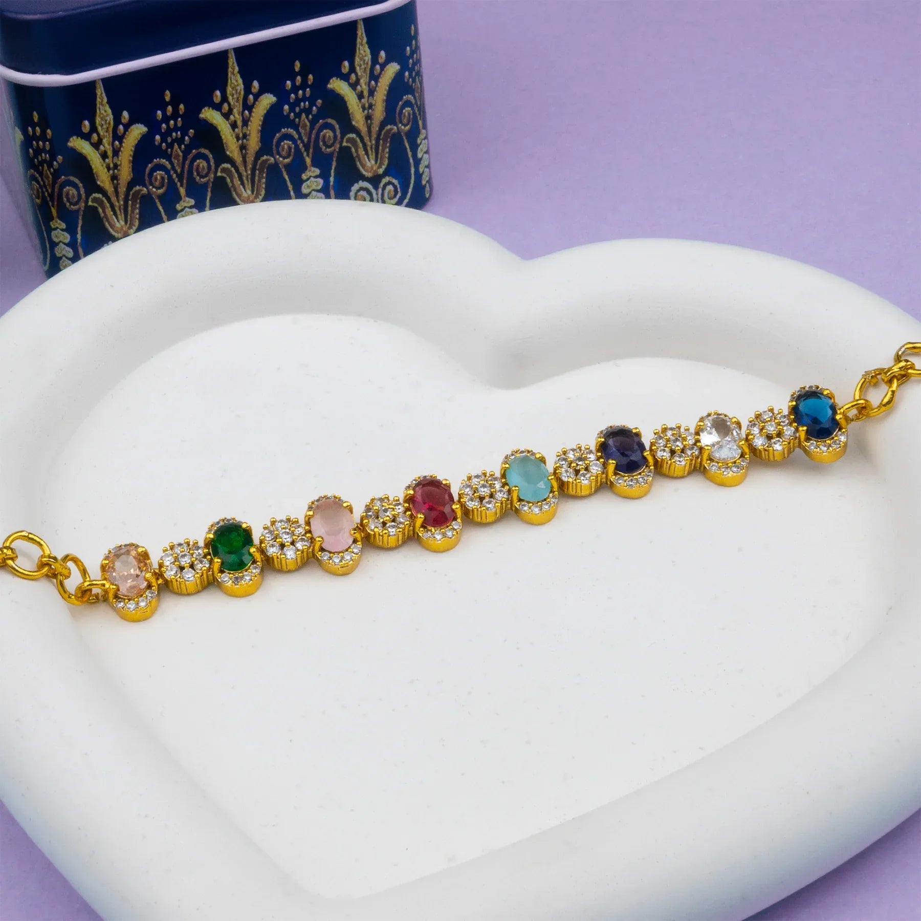Gold bracelet with colorful gemstones on a white heart-shaped stand with a purple background