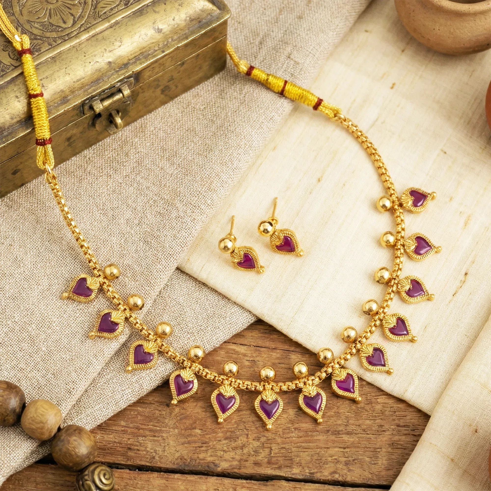 Gold necklace with purple heart pendants and matching earrings on a textured surface.