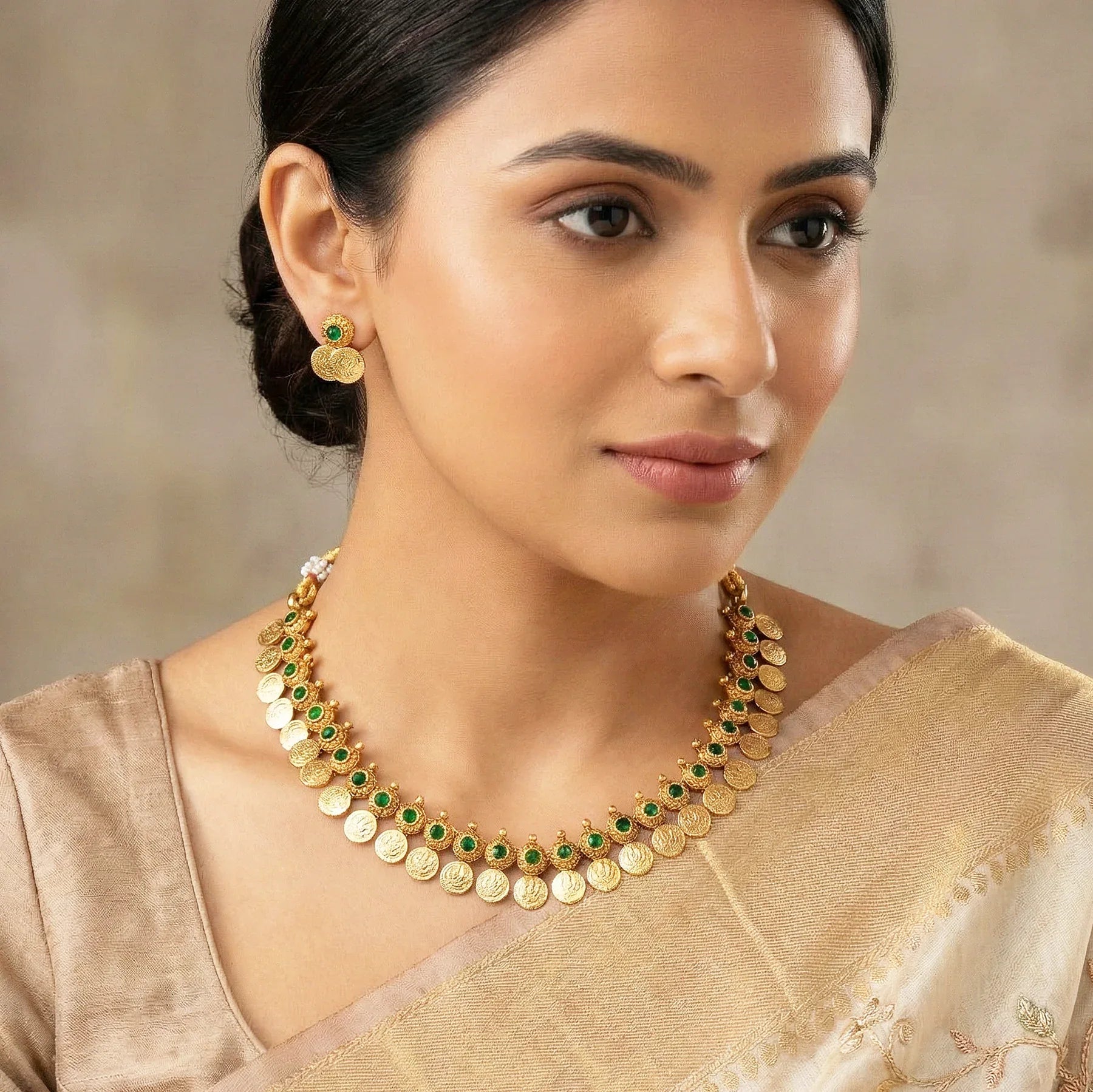 Woman wearing a gold necklace with green stones and earrings.
