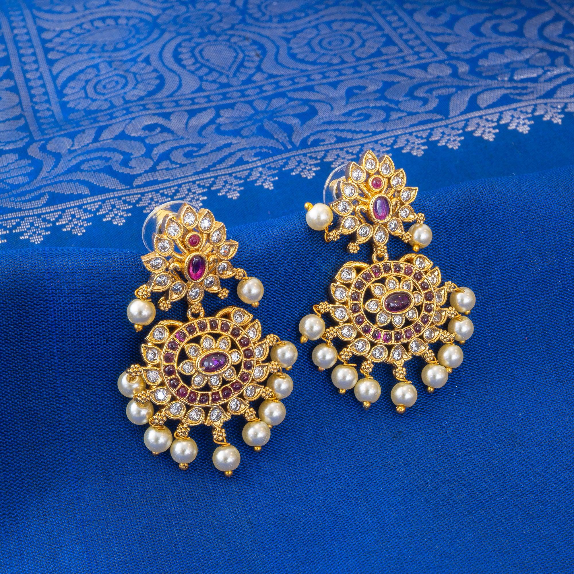 Ornate gold earrings with pearls and red stones on a blue fabric background