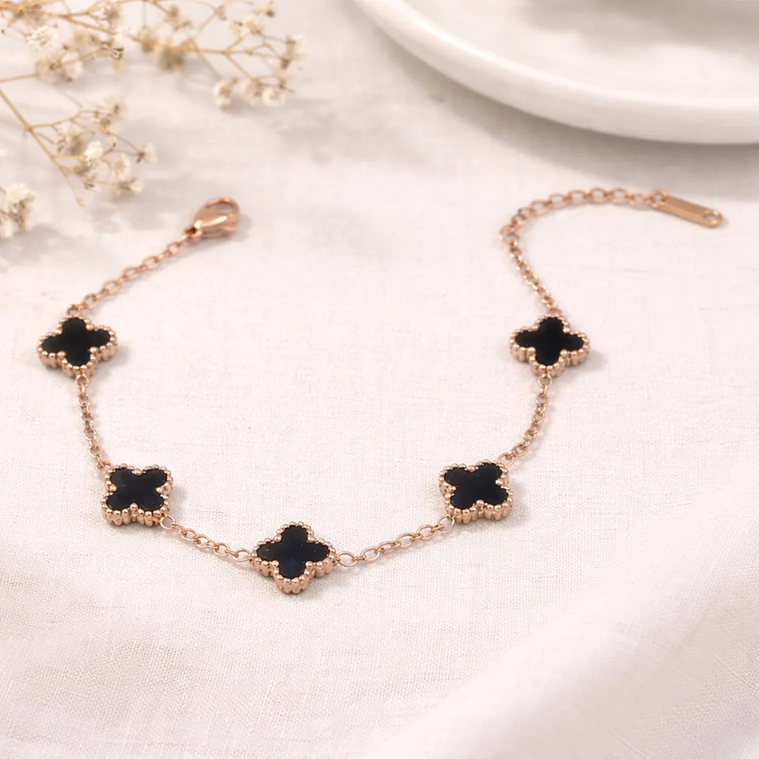 Rose gold necklace with black clover-shaped pendants on a white surface with small flowers.