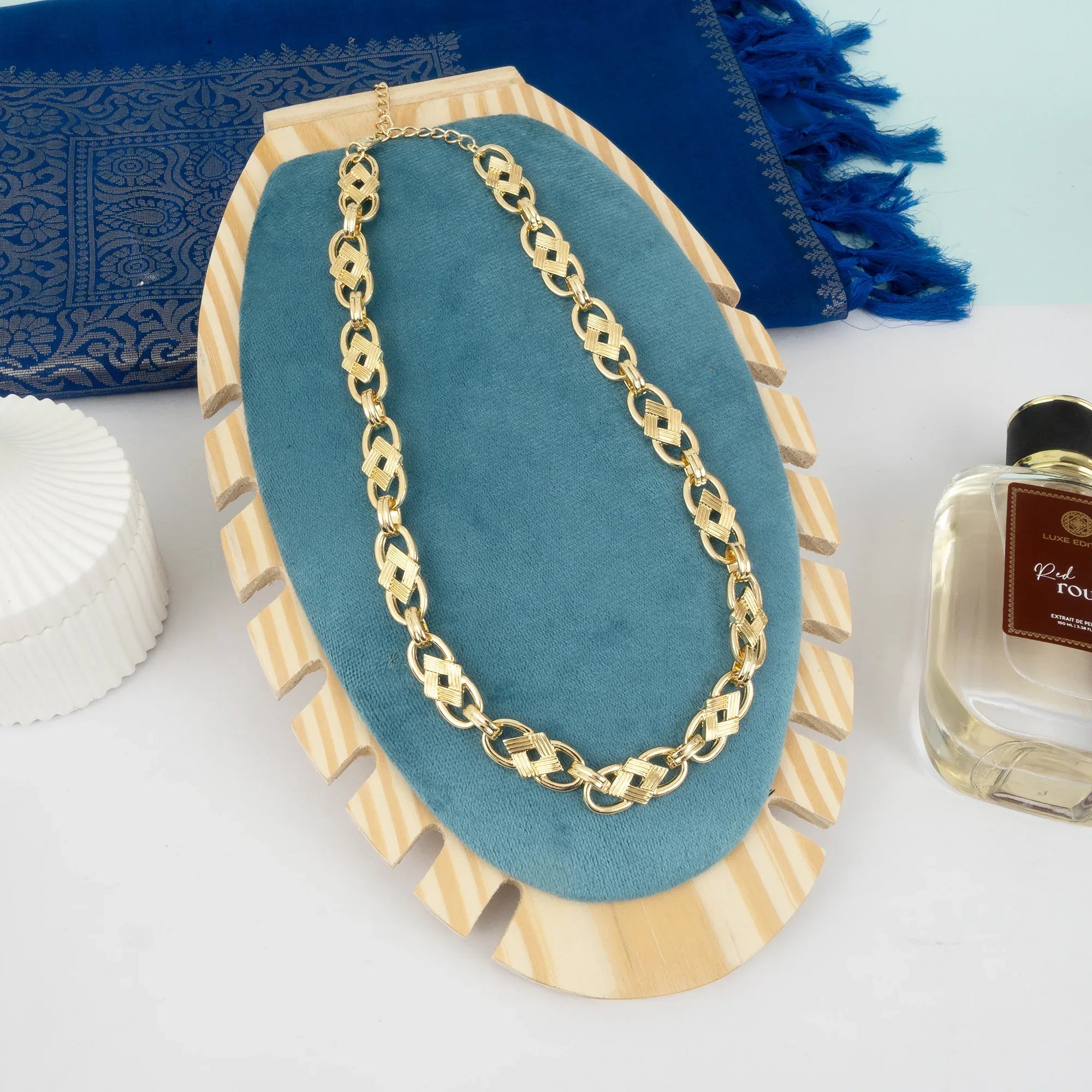 Gold chain necklace on a blue cushion with a perfume bottle in the background