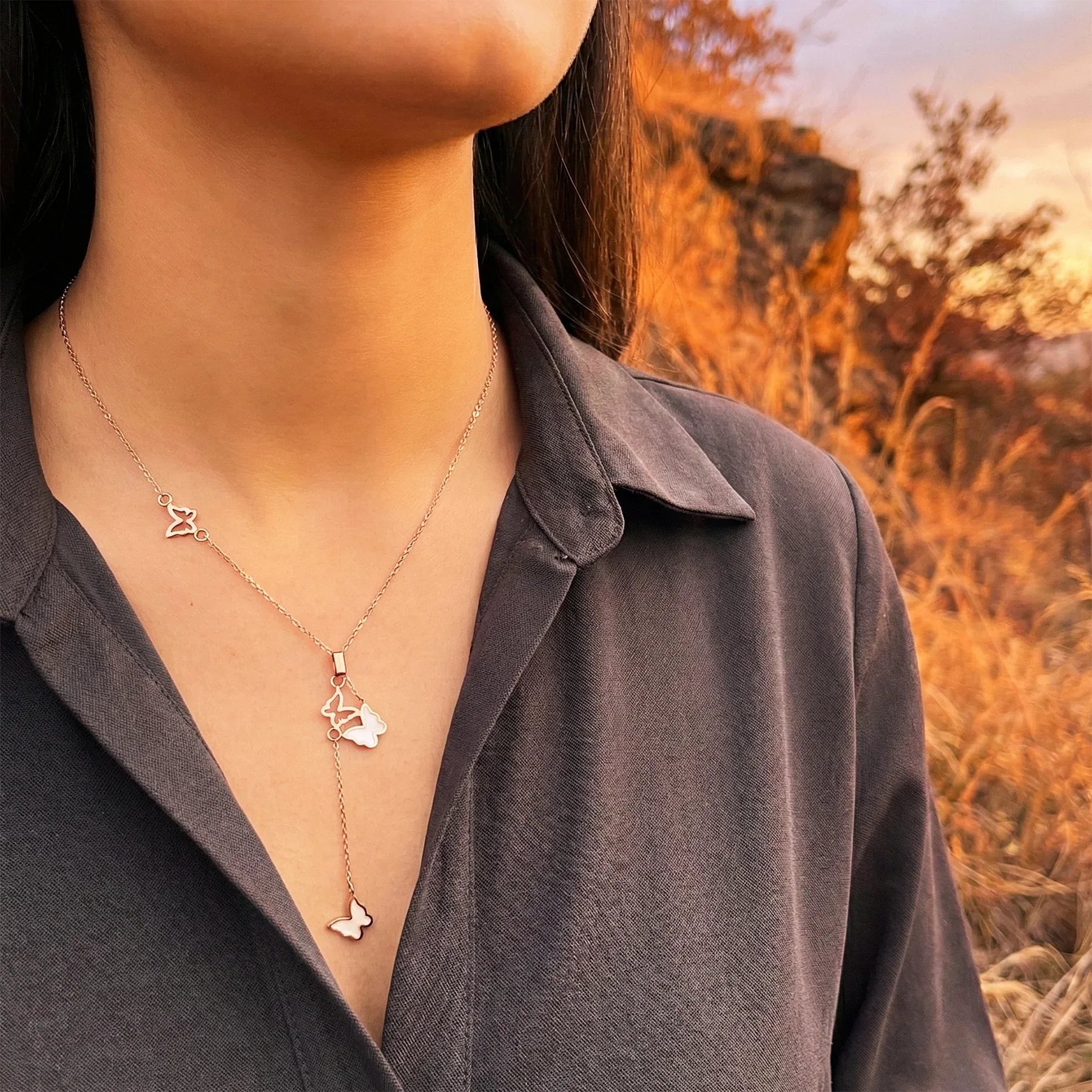 Person wearing a necklace with butterfly pendants against a blurred natural background