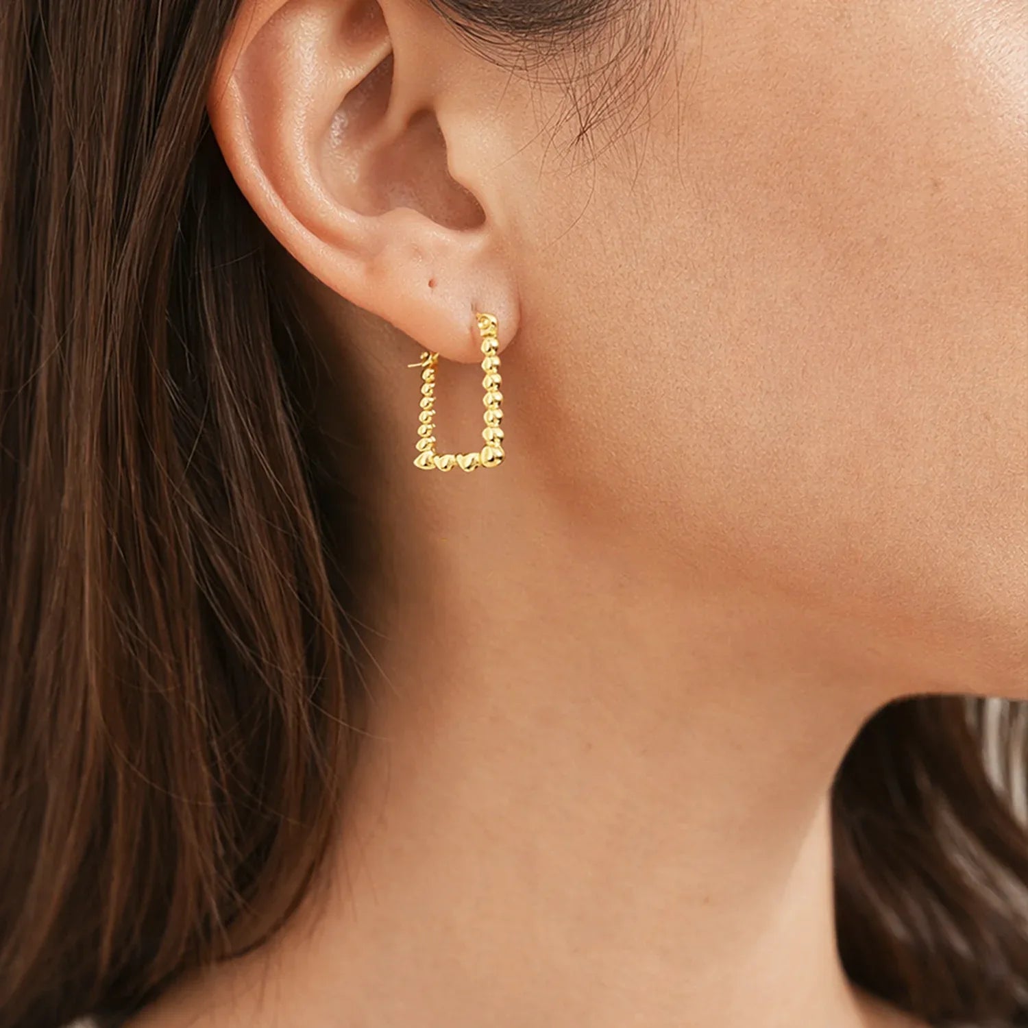 Gold hoop earrings worn by a person with brown hair.