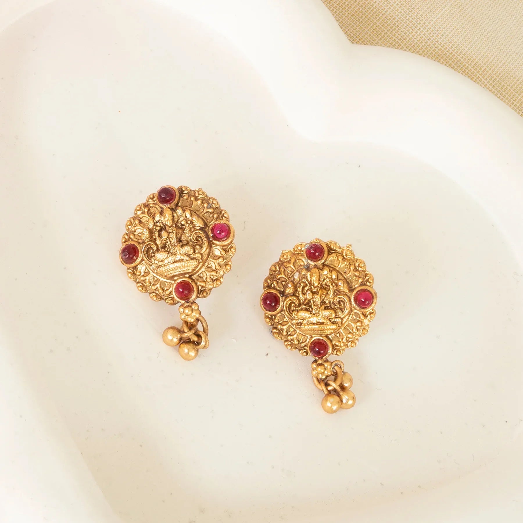Gold earrings with red gemstones on a beige fabric background