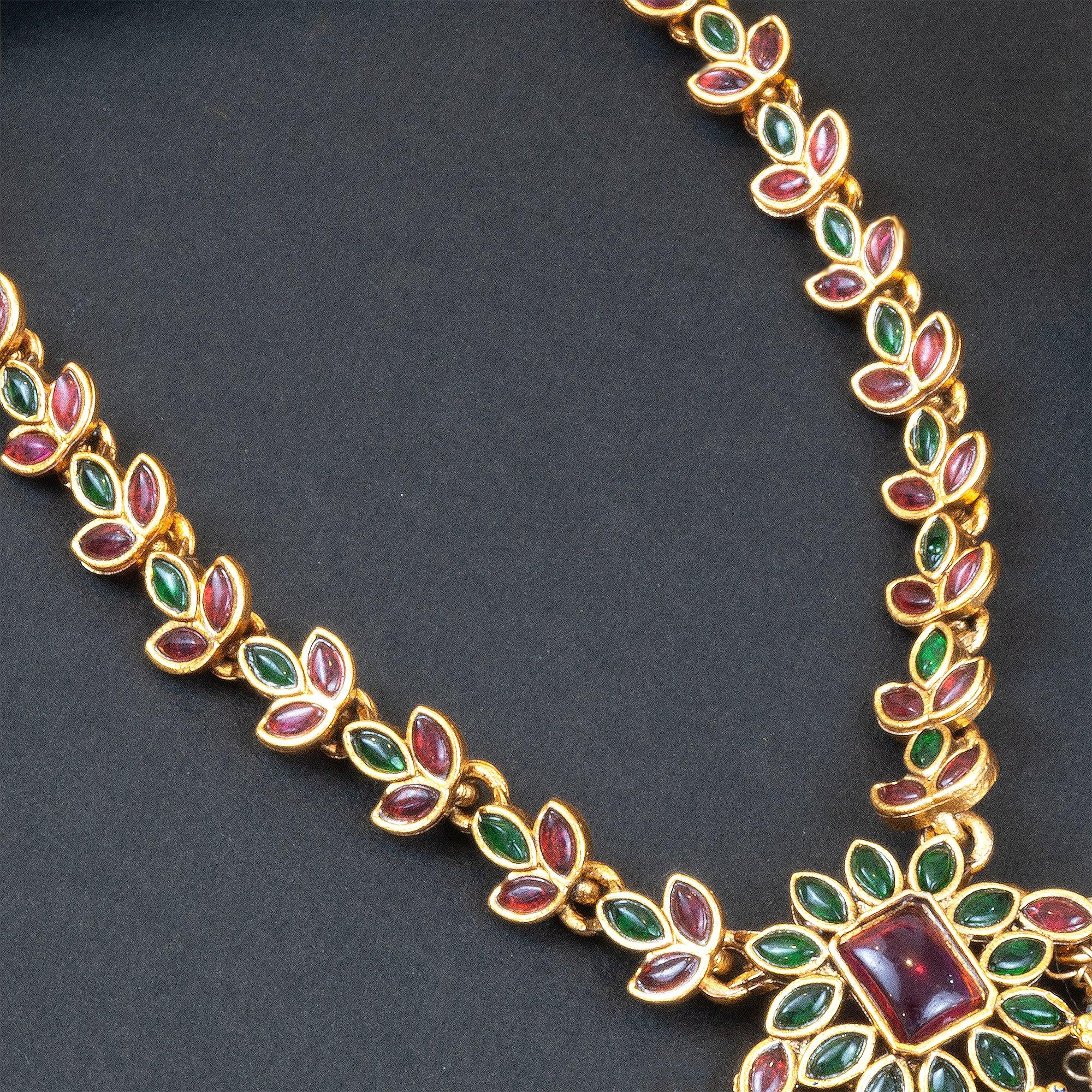 Gold necklace with red and green gemstones on a dark background