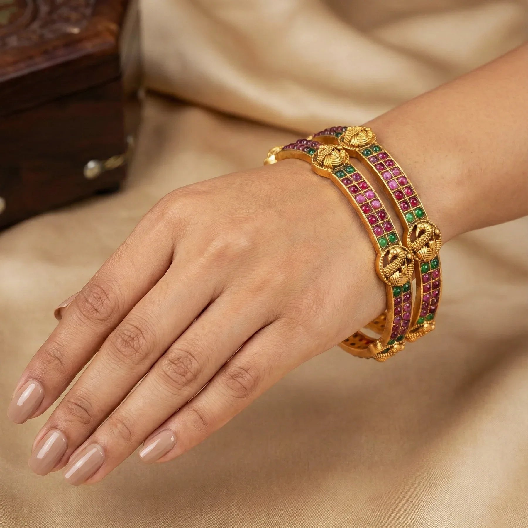 Gold bracelet with colorful stones on a hand against a neutral background