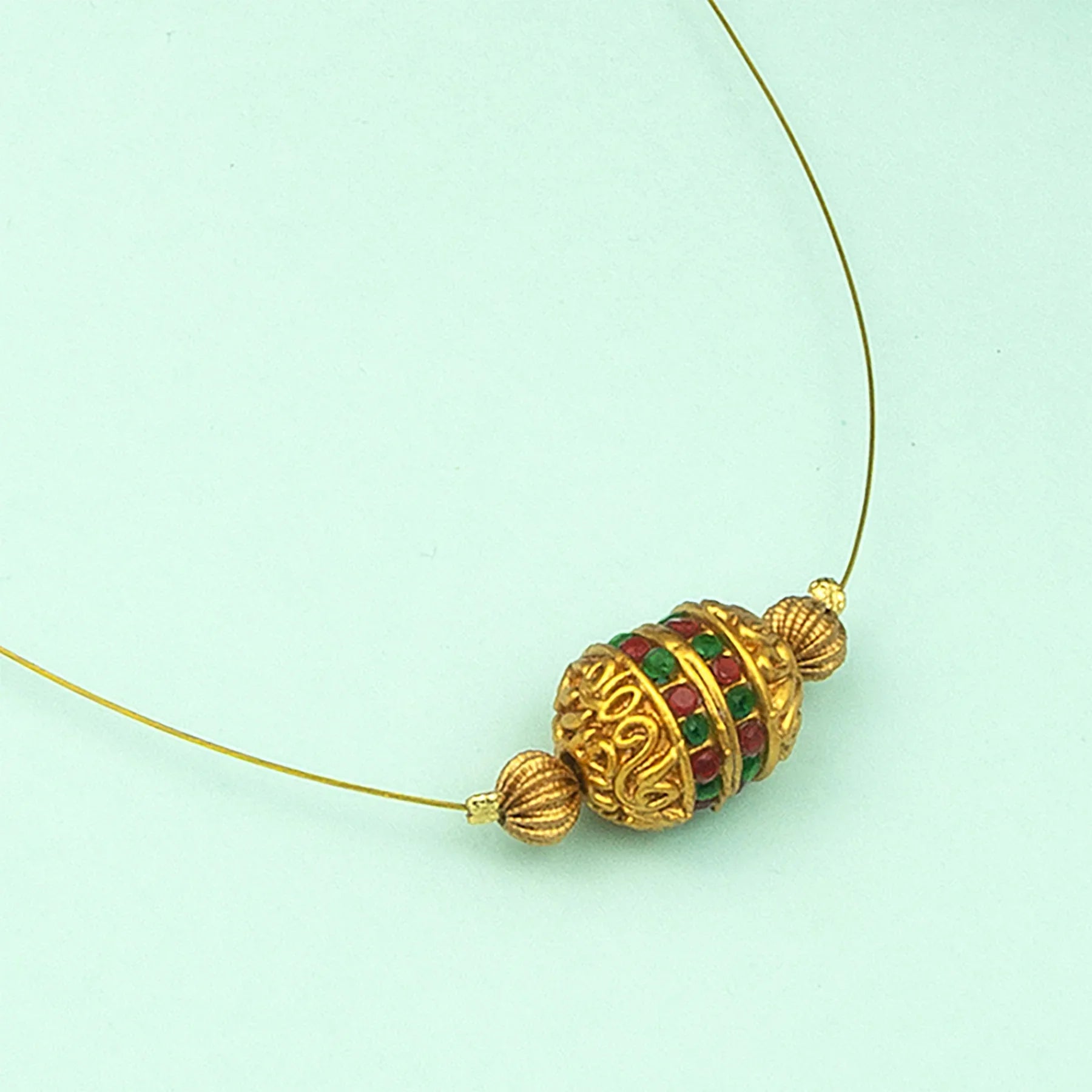 Gold necklace with a decorative bead on a light green background