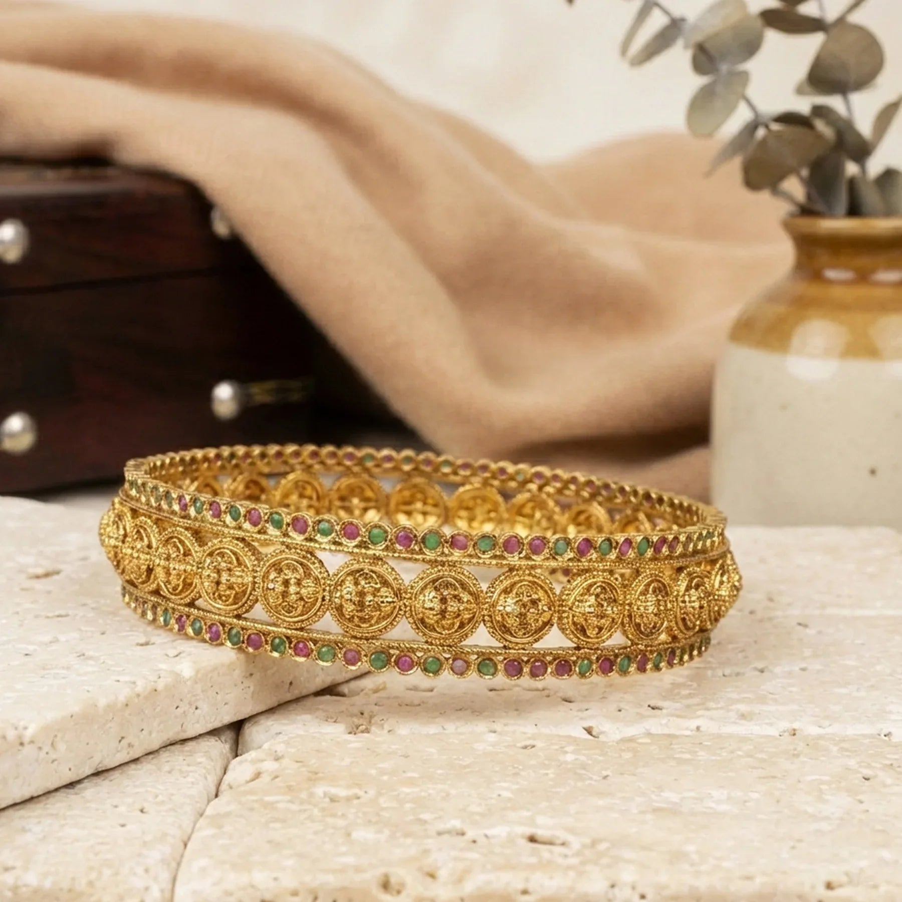 Gold bracelet with colorful stones on a textured surface with a blurred background