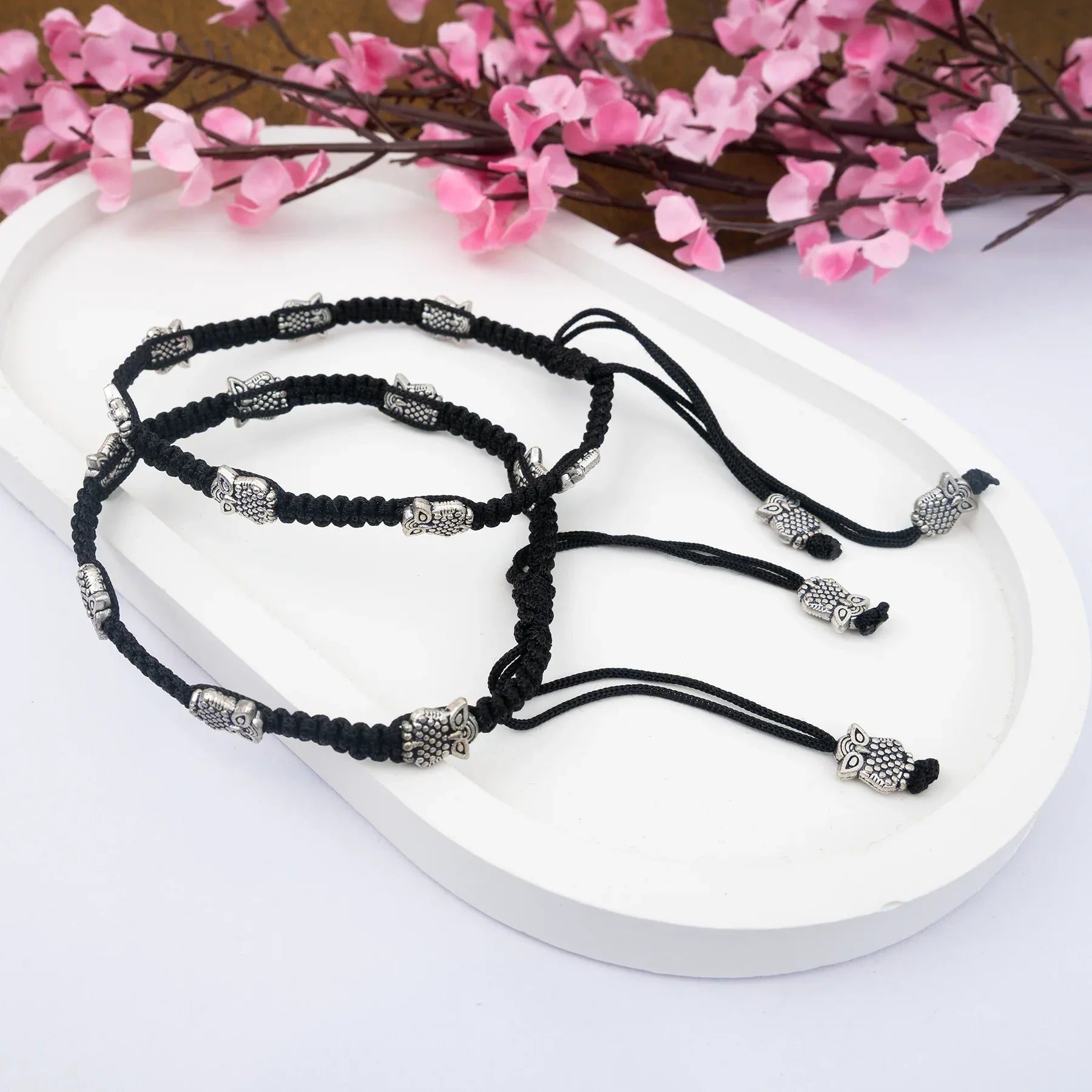 Black bracelets with silver beads on a white surface with pink flowers in the background