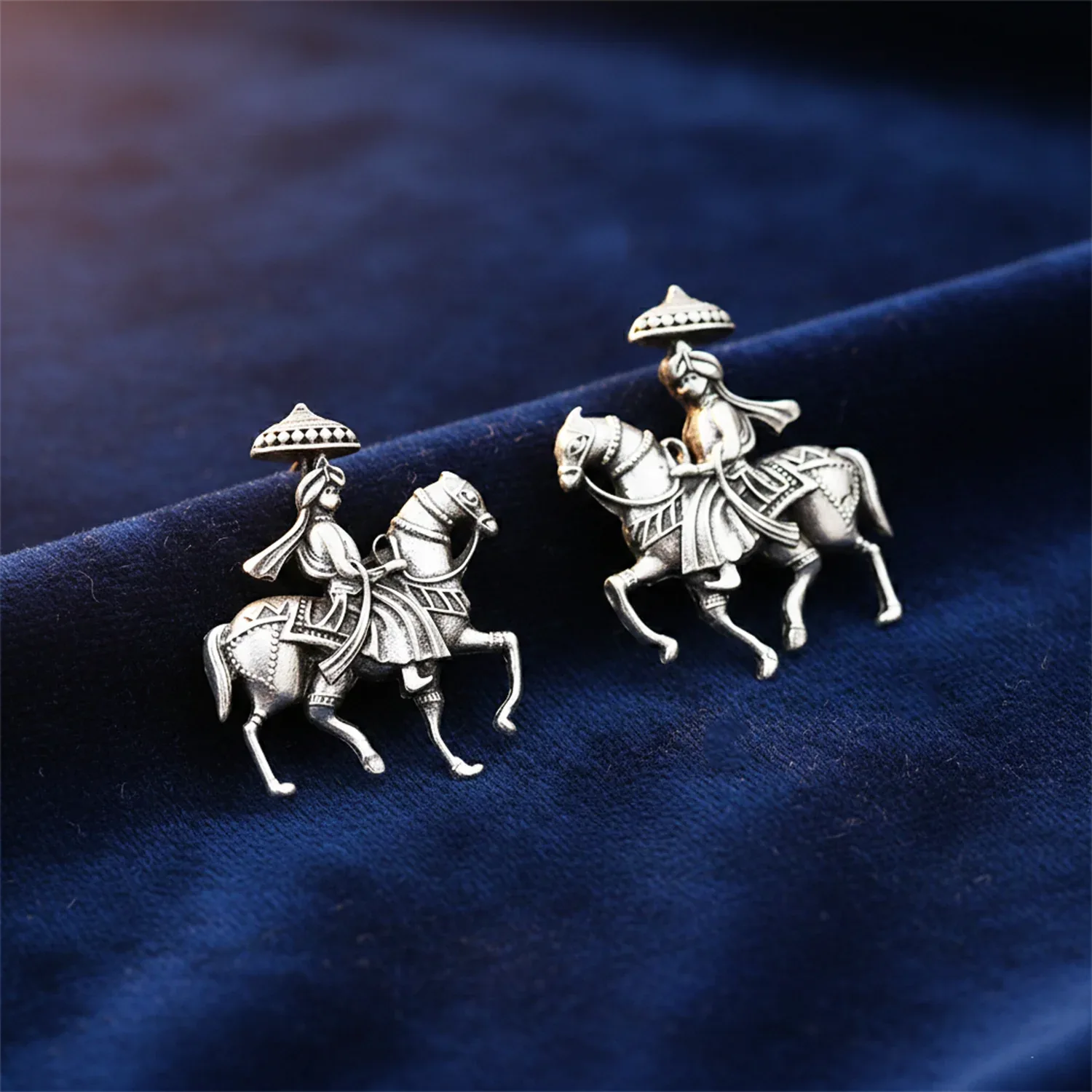 Silver earring with a design of a person on horseback on a blue fabric background