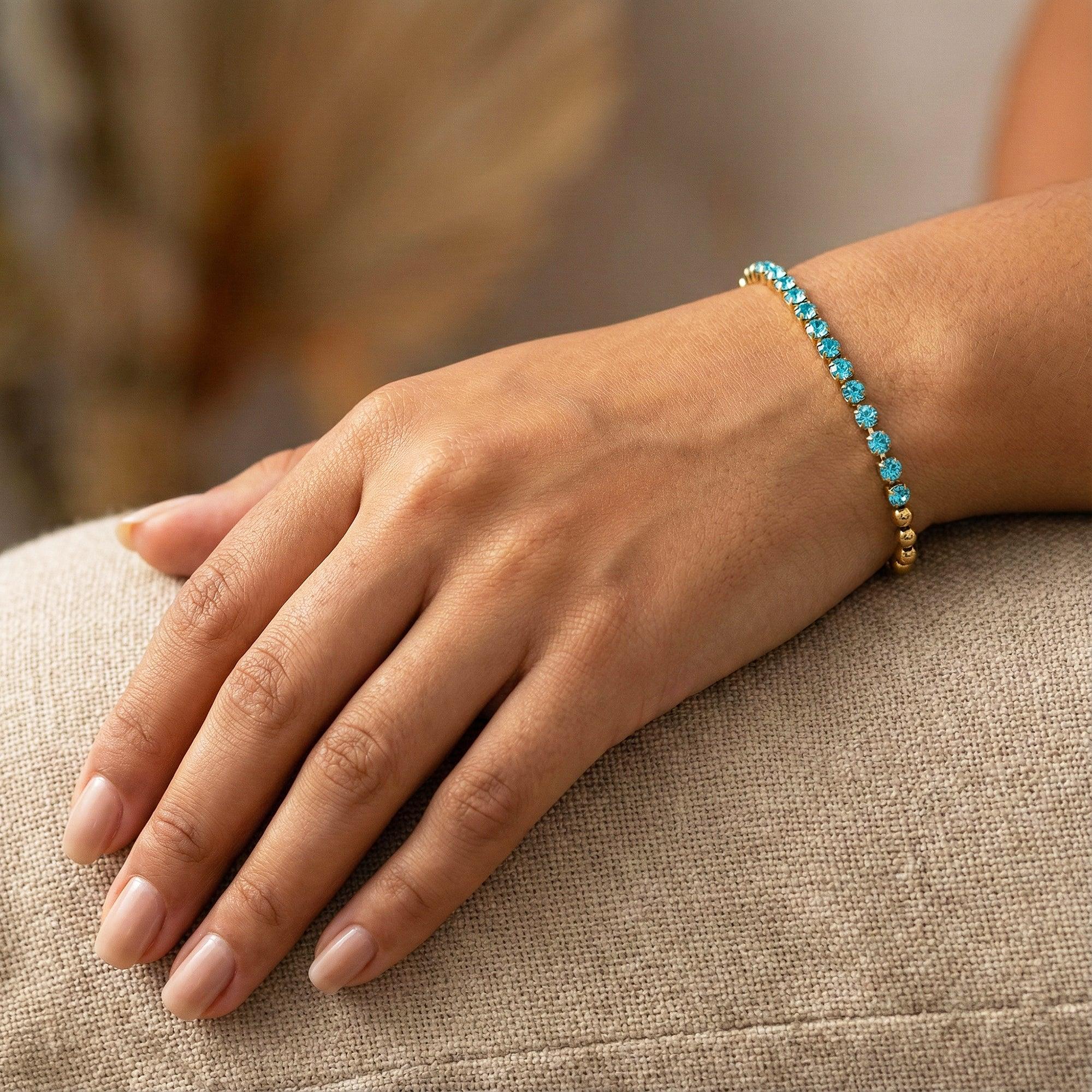 Hand wearing a turquoise beaded bracelet on a neutral background