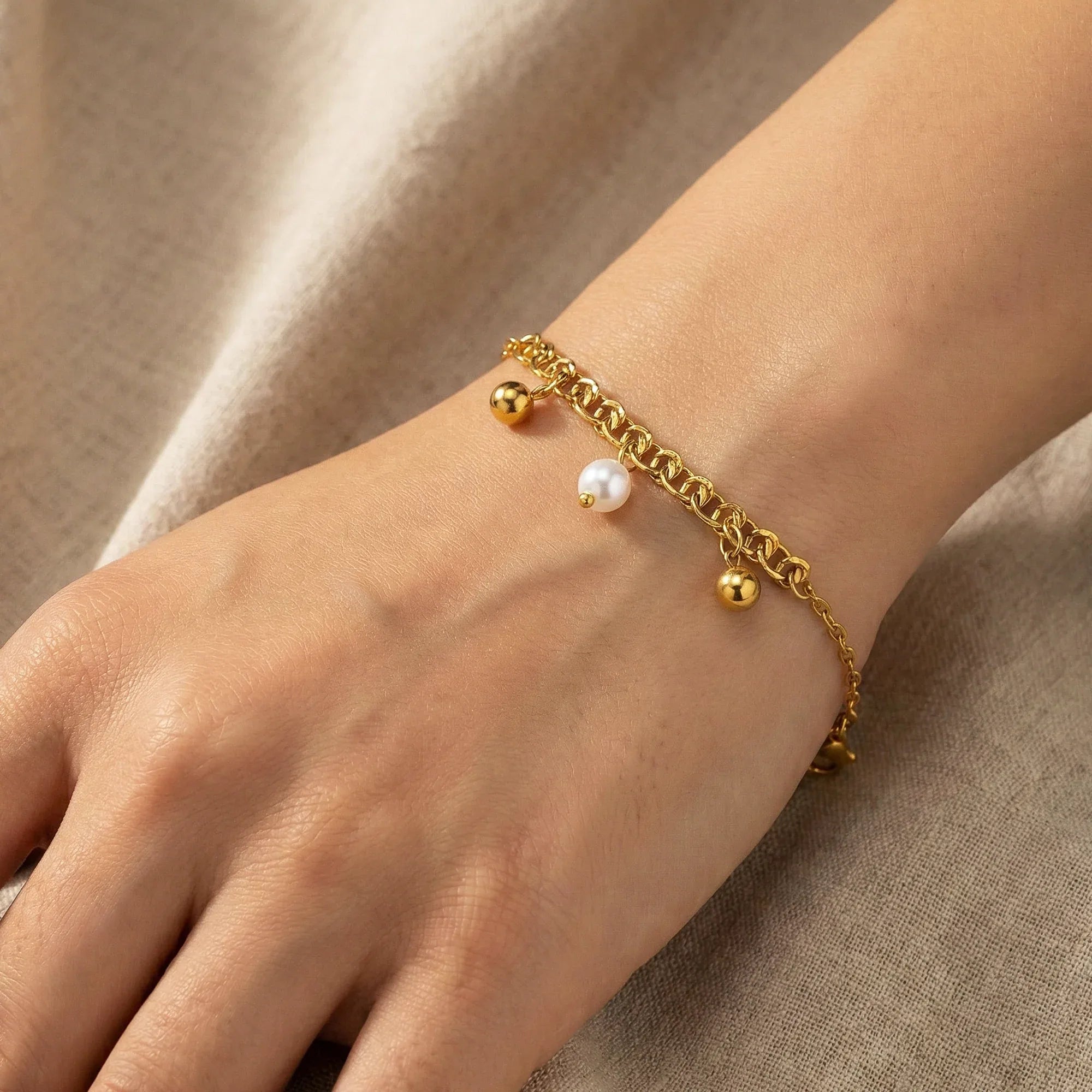 Gold bracelet with beads on a wrist against a beige fabric background