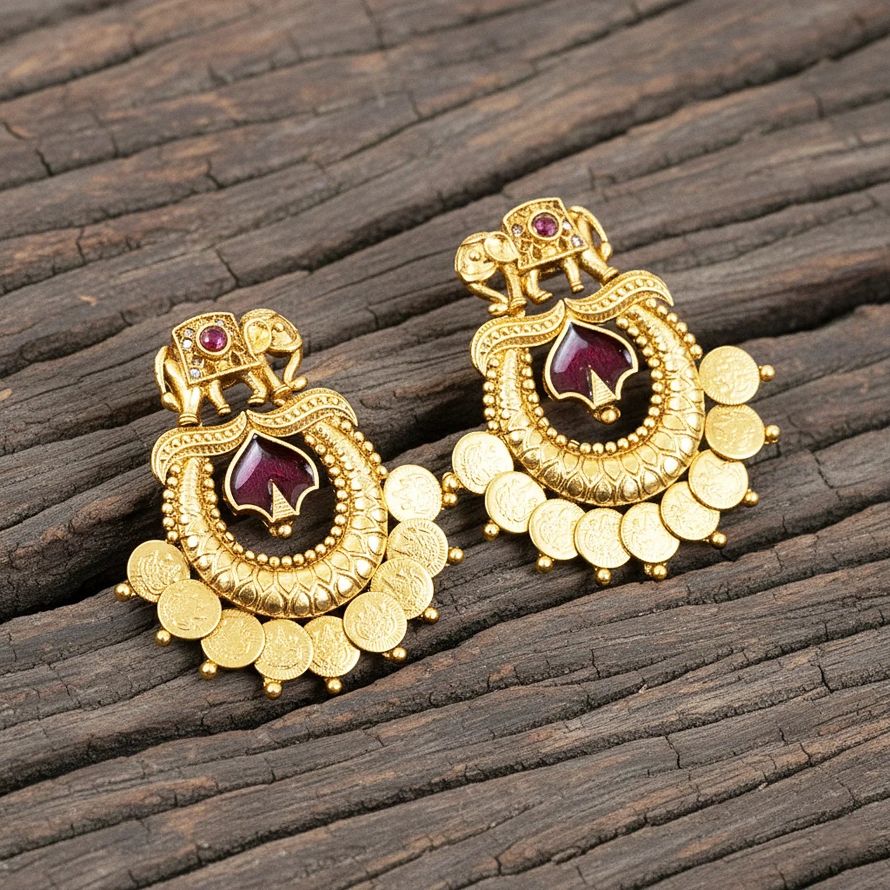 Gold earrings with red gemstones on a wooden surface